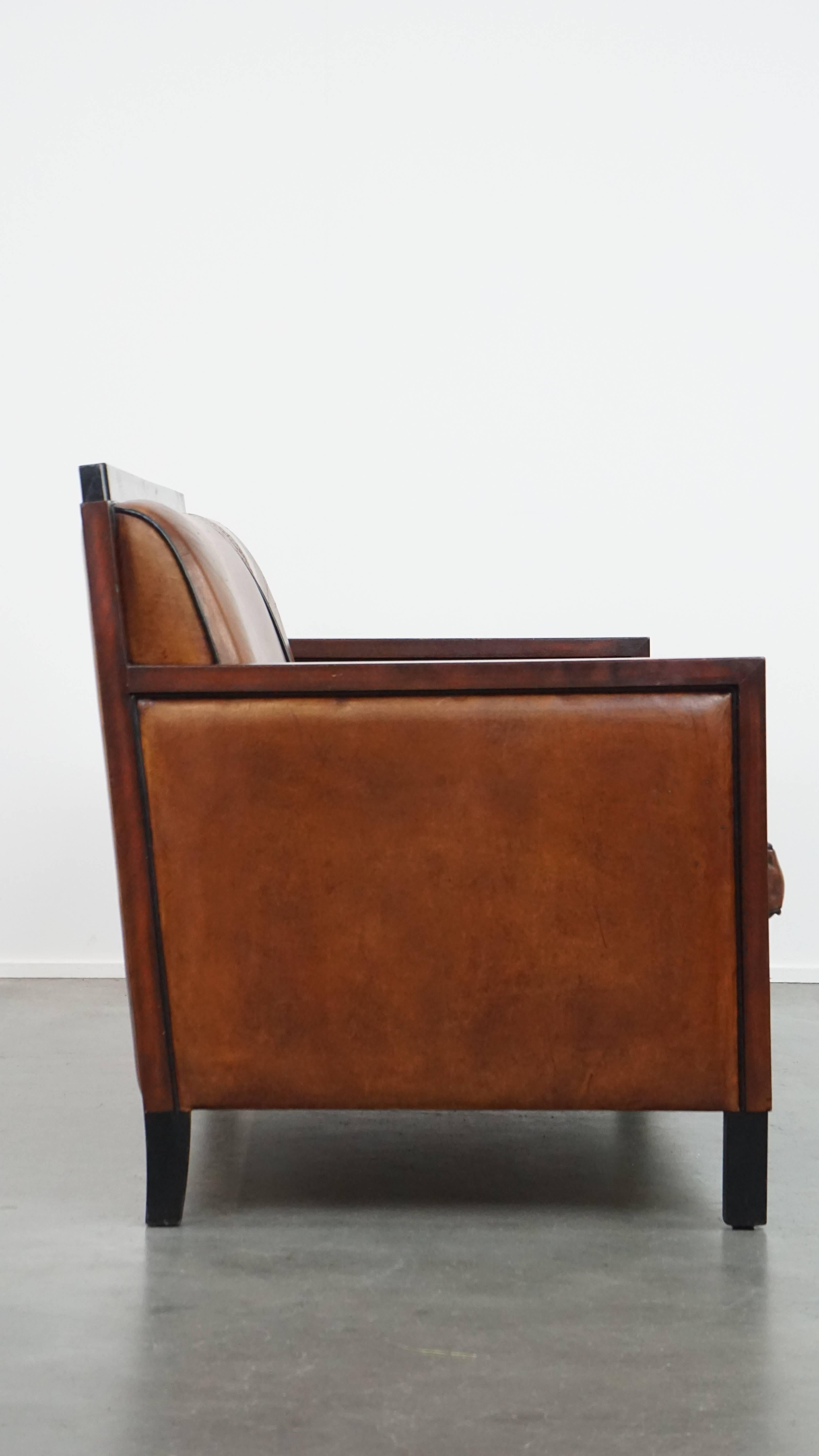 Angeboten wird dieses atemberaubende Zweisitzer-Sofa im Art-Déco-Design aus Schafsleder mit Armlehnen aus Holz und eleganten schwarzen Paspeln. 

Dieses stilvolle Art-Déco-Sofa ist ein echtes Charakterstück, das sich nahtlos in fast jedes Interieur