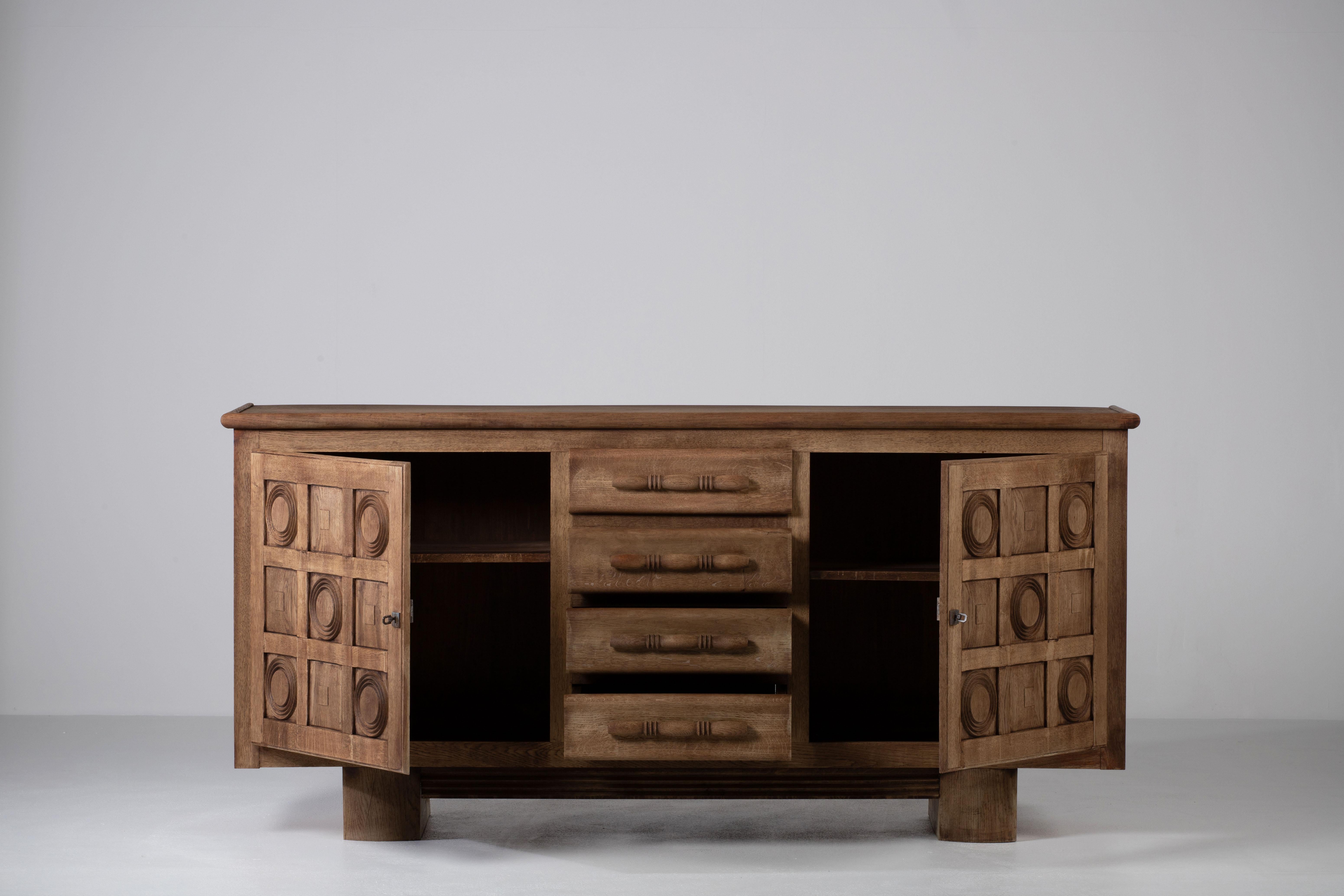 Credenza, solid oak, France, 1940s, after Charles Dudouyt.
Large Art Deco Brutalist sideboard. 
The credenza consists of three central drawers and two storage facilities and covered with very detailed designed doors. 
The refined wooden