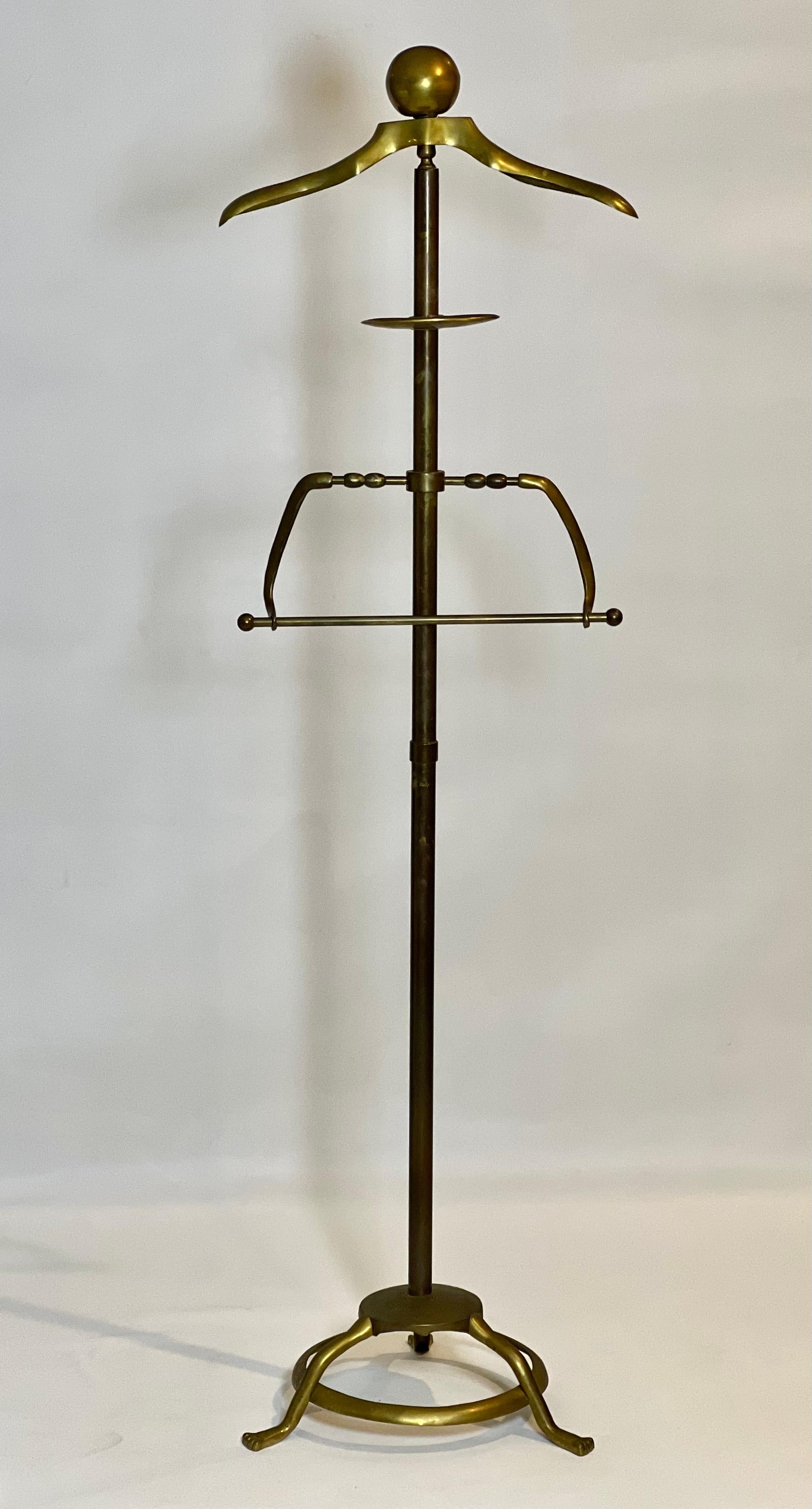 Art Deco solid brass valet stand, c. 1960s.

Elegant valet stand with pant hanger, small tray for accessories and contoured shoulder form hanger.   It features three stylized feet on a circular base and a large ball finial.  The pant hanger can