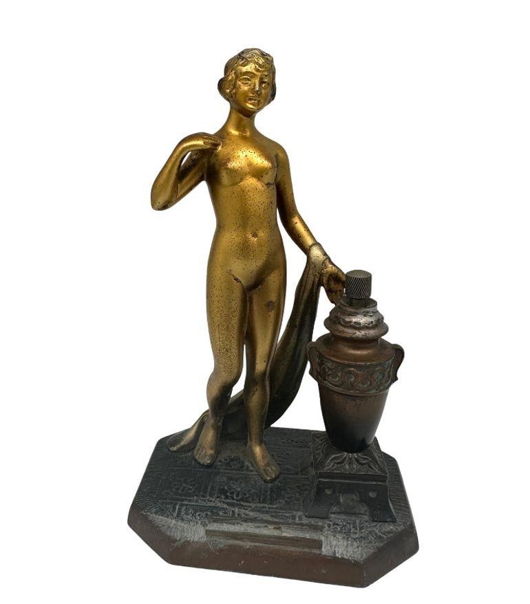 Accendino da tavolo con punta a torcia in metallo spelta con una dea greca nuda dorata in bronzo. L'urna accanto alla divinità contiene l'olio e il percussore con il supporto per la pietra focaia nella fortezza.

Misure: 4