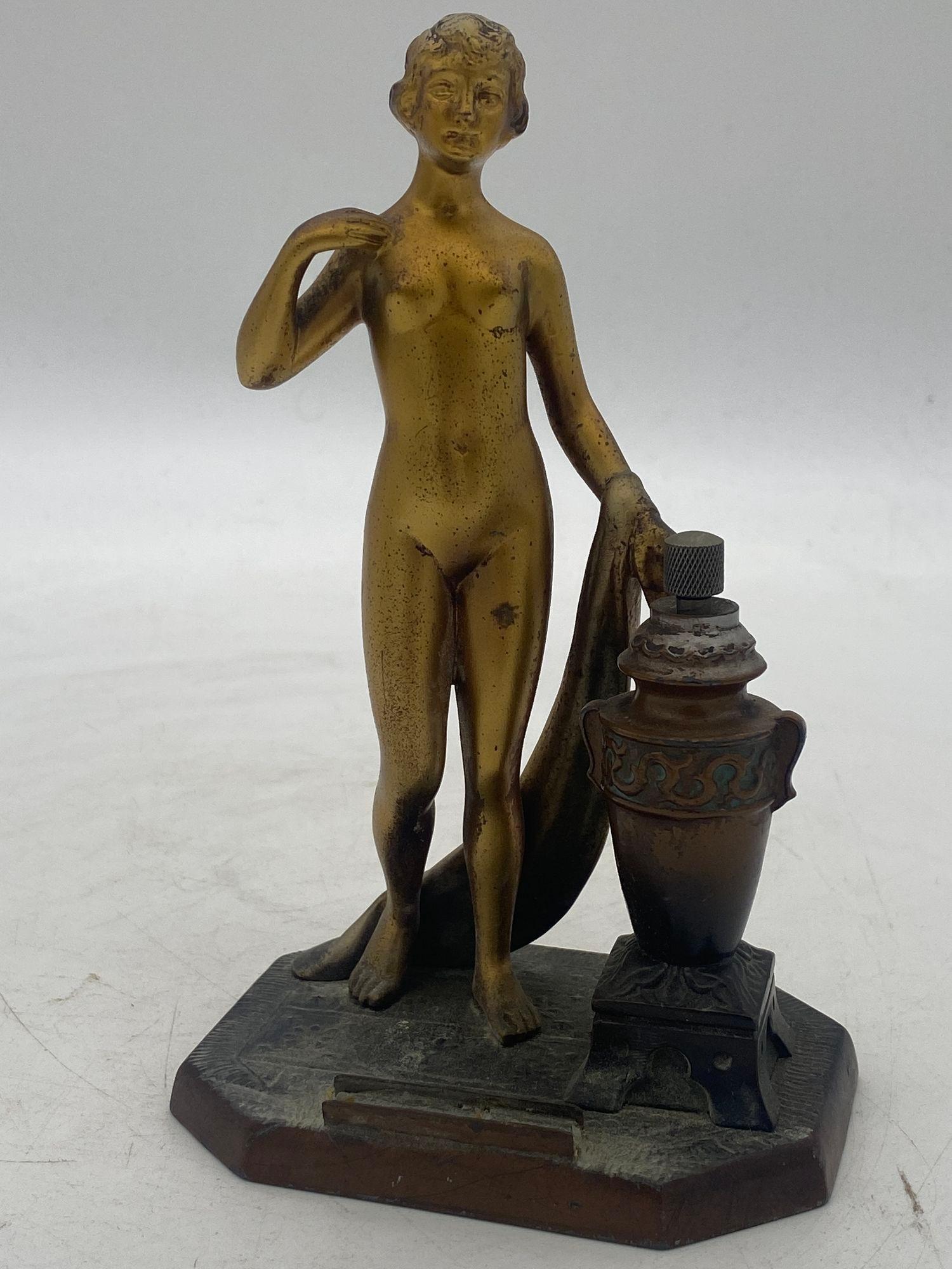 Nude Greek Goddess spelter metal torch tip table lighter featuring a nude flapper gilded in bronze. The urn next to her contains the oil and striker with the holder for the flit in fort.

Circa 1930