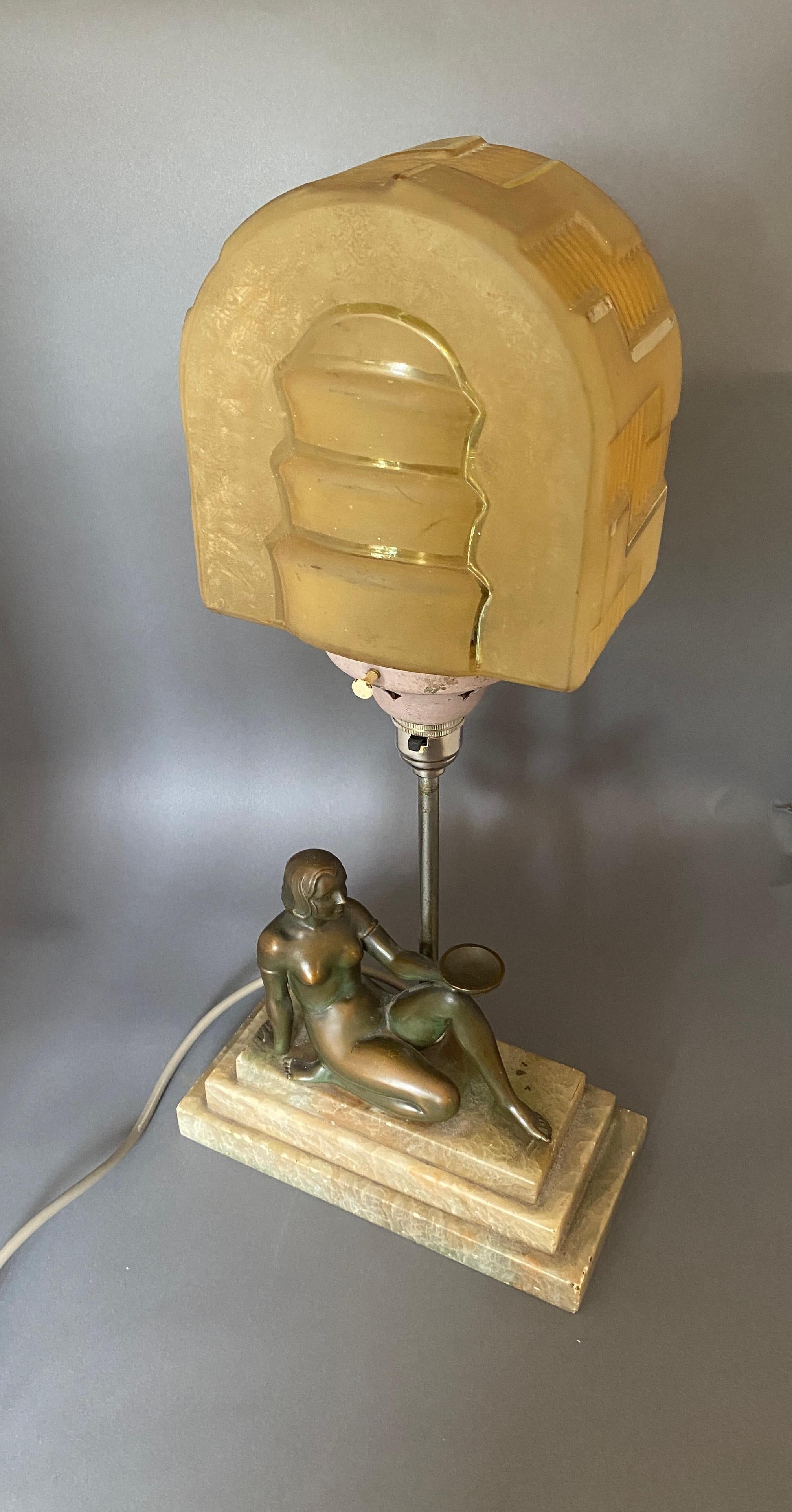 Lampe de dame art déco en fonte,

Figure de dame en fer forgé assise sur une base en onyx à gradins, 

Colonne plaquée supportant un porte-lampe plaqué nickel, 

Support d'abat-jour peint, avec abat-jour original en verre teinté or avec détails