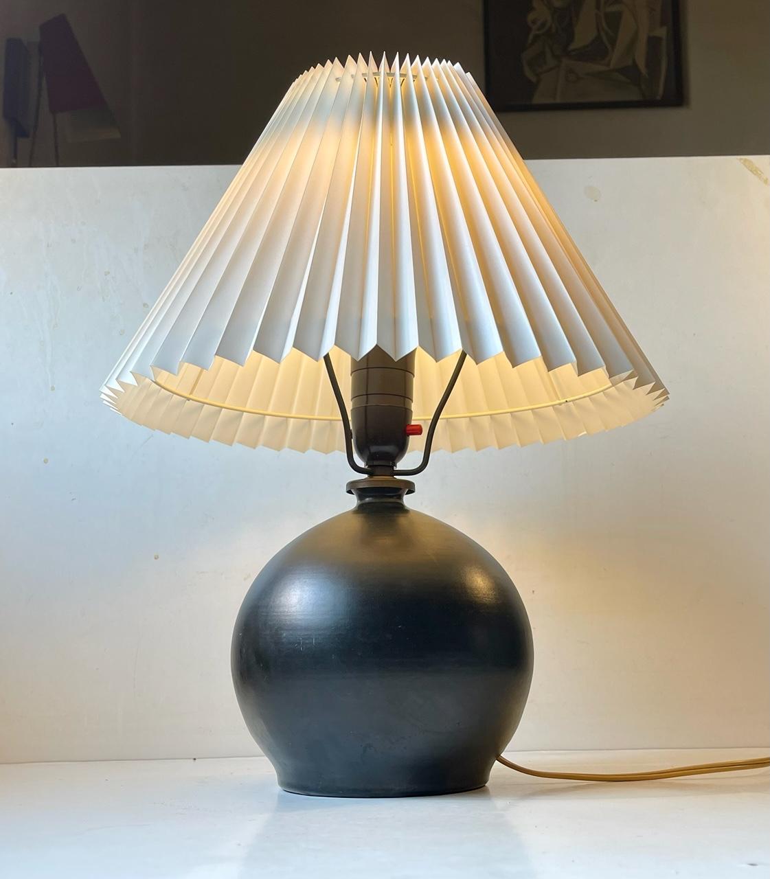 Lampe de table sphérique en céramique dans le style de Jean Besnard. Elle présente une glaçure noire satinée profonde, une douille en bakélite d'origine avec un interrupteur à broche et des ferrures en bronze. Il a été conçu et créé à Copenhagen