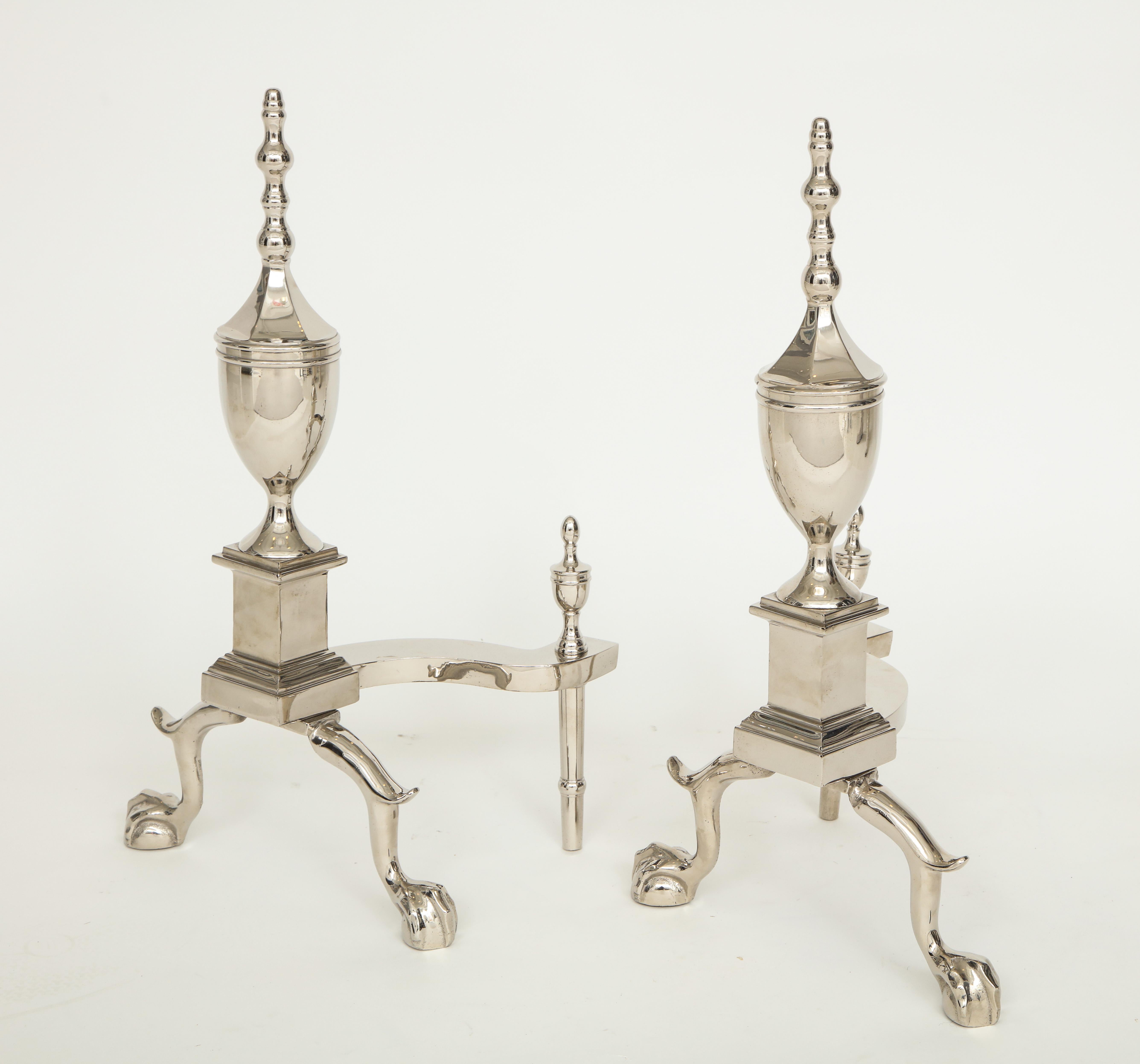 Pair of Art Deco polished nickel andirons featuring classical urn shaped body, claw with ball feet and topped by a spire finials.