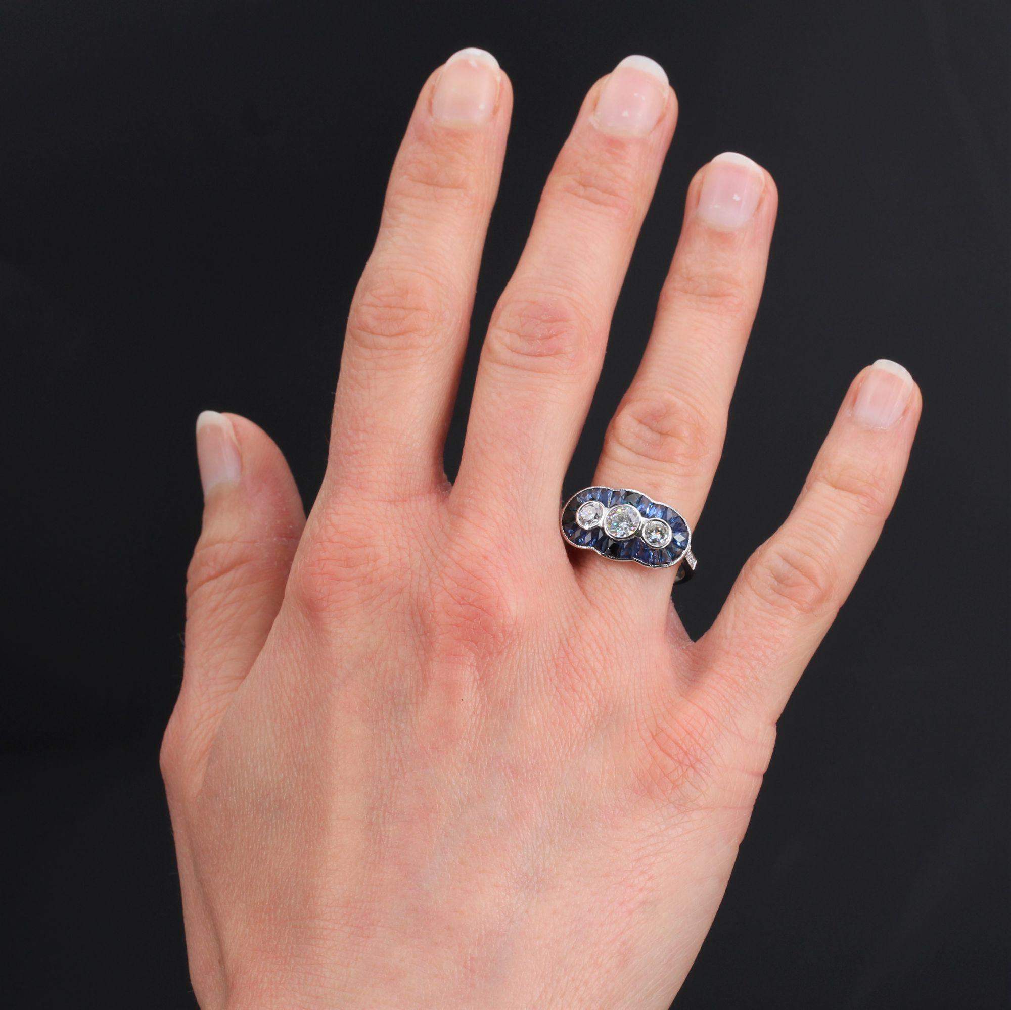 Ring in 18 karat white gold, eagle head hallmark.
A lovely modern Art Deco style ring, it is set with three modern brilliant-cut diamonds in a poly-lobed setting of calibrated sapphires on top. On either side, on the start of the ring are set 2x4