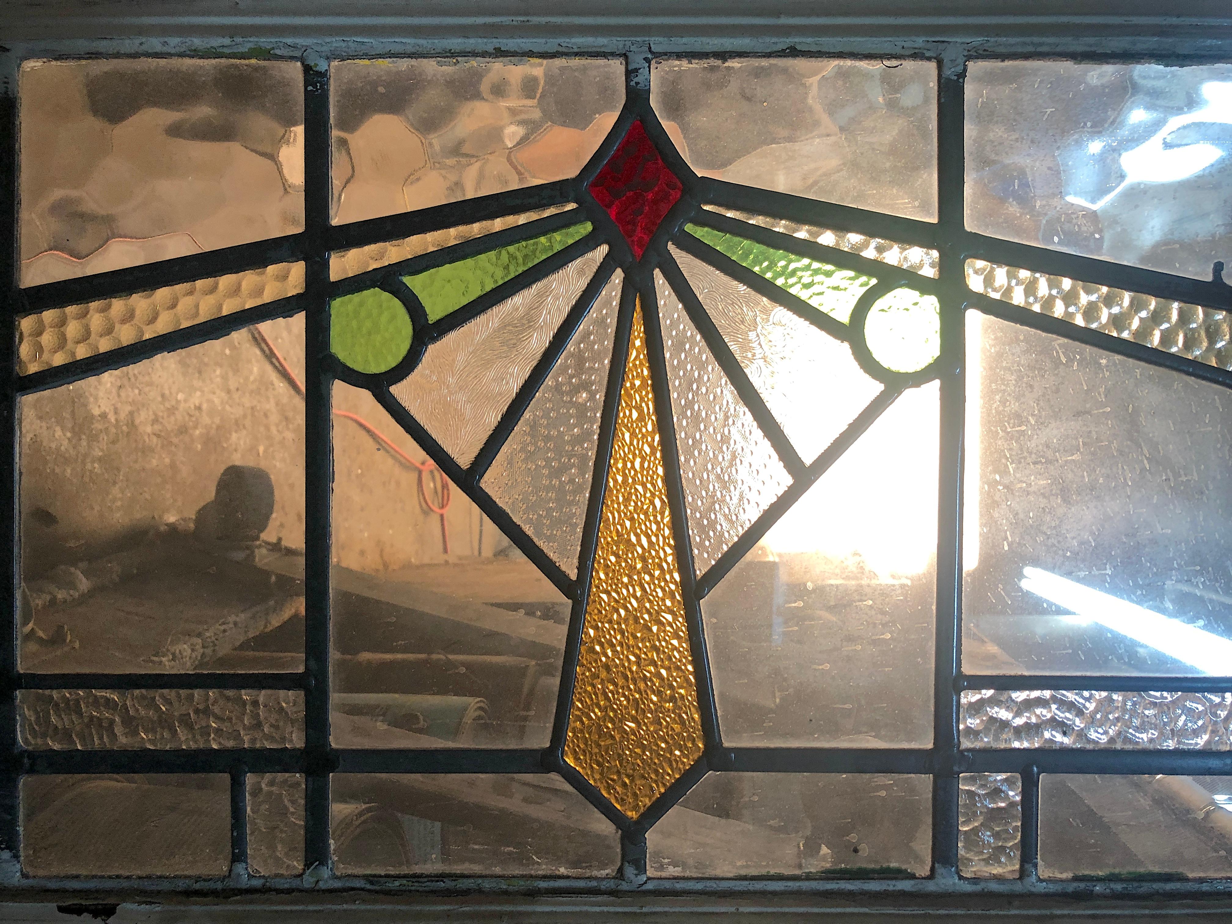 Long stained glass transom window with Art Deco geometric designs. A mix of textured glass panels in clear, yellow, reg and green coloring.
Currently housed in a wooden frame - the overall dimensions are for the stained glass and the frame.
Located