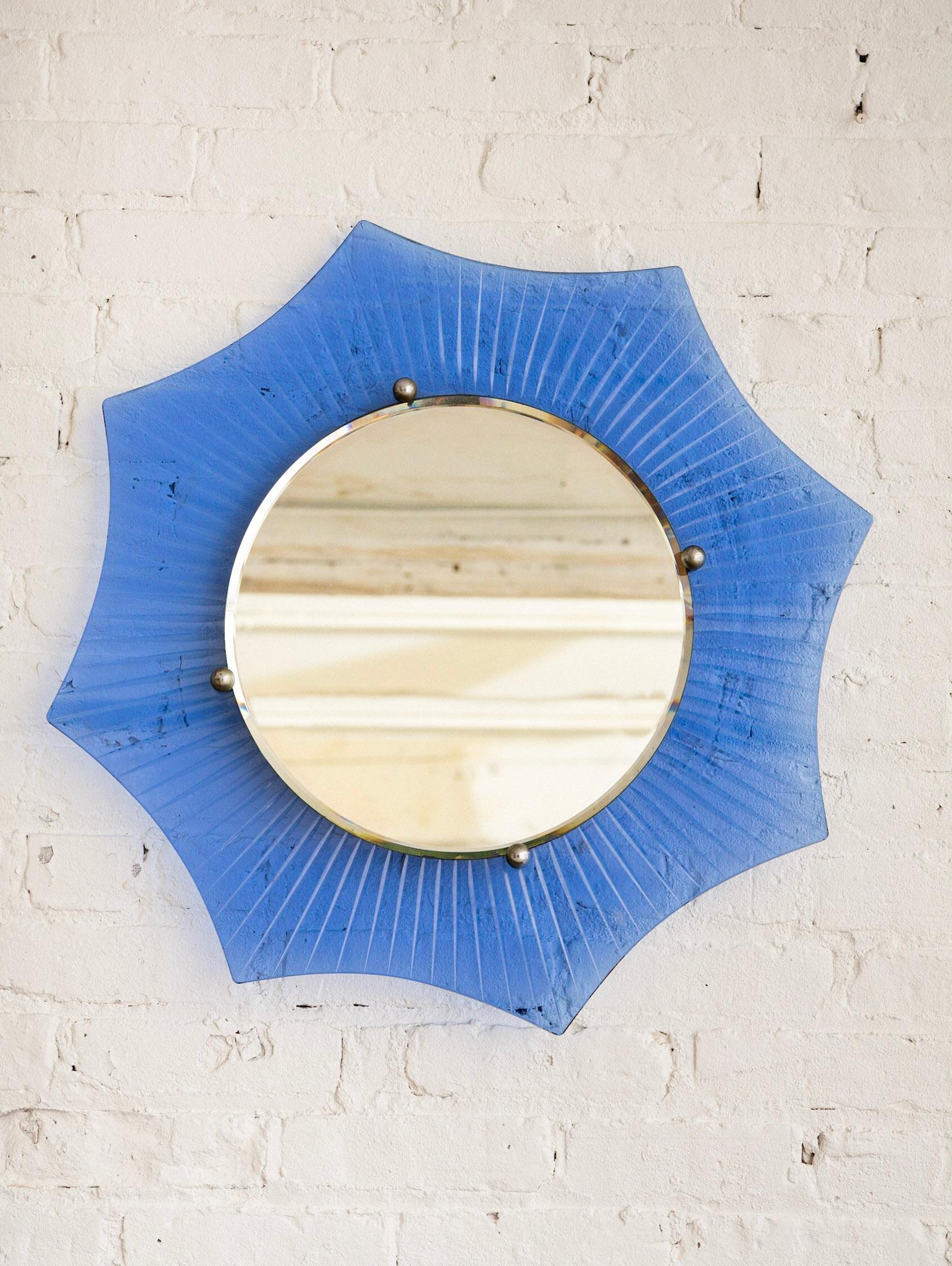 Art Deco starburst form mirror. Outer scalloped edge cobalt glass etched with a starburst pattern. Inner beveled mirror held in place with round chrome caps.