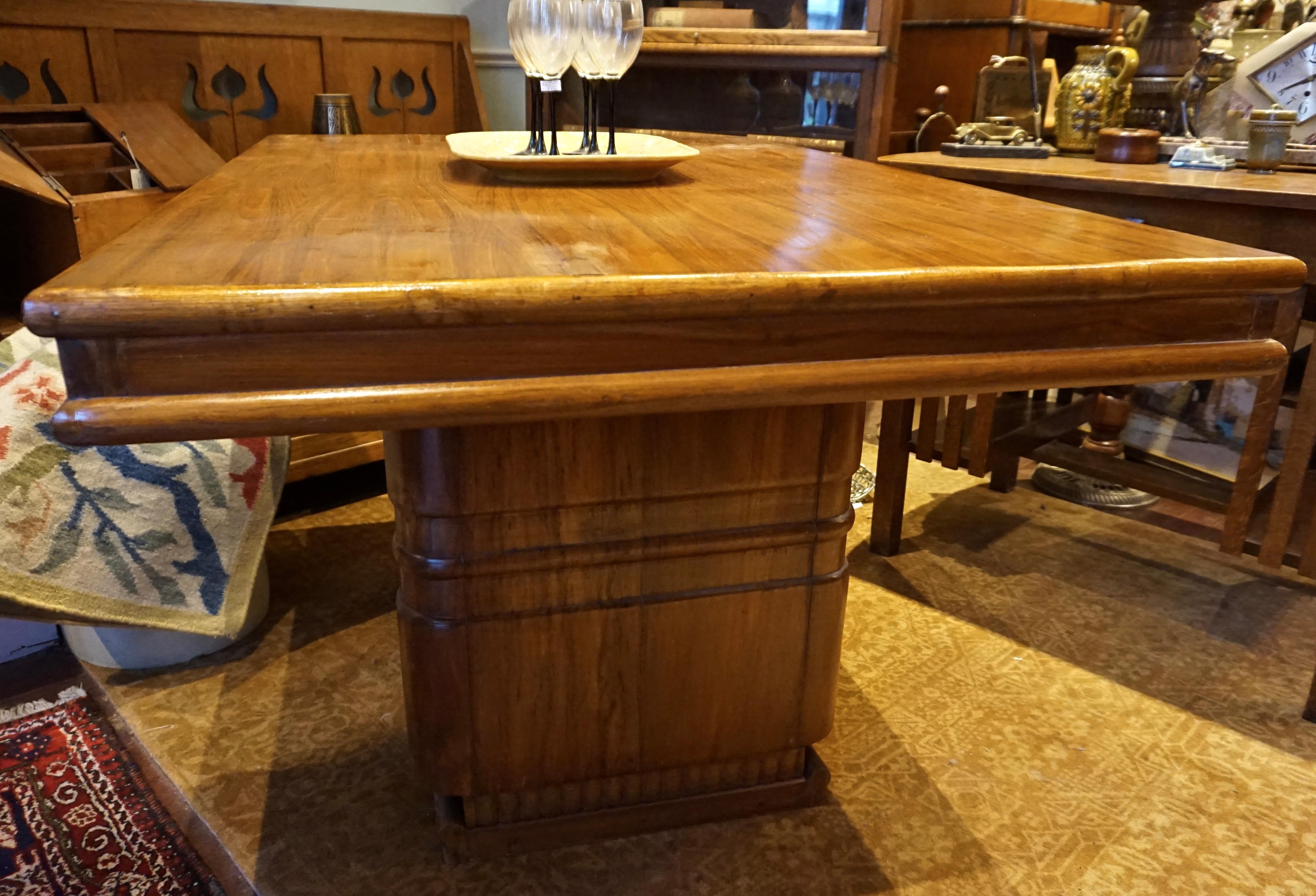 Solid teak dining table from the Deco era with a beautiful veneer top showing free flowing honey grain. The table top sits on two broad legs that resemble steamship chimneys from the era. Latch mechanism secures top to legs. Handsome and versatile.