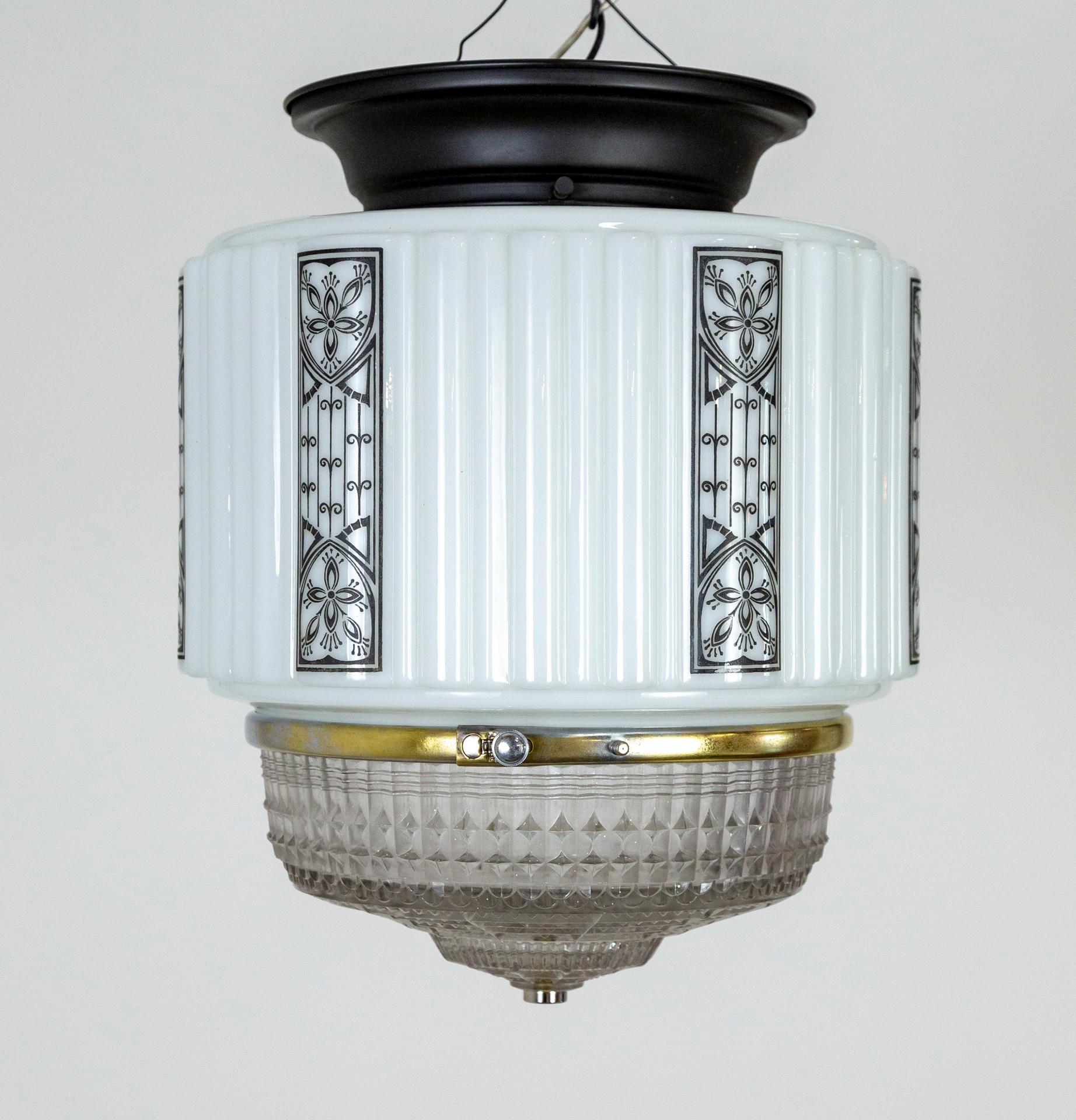 A flush mount ceiling light made of milk glass in a cylindrical form with columns of stenciled black Deco patterns; and a textured, molded, clear glass diffuser. It has a black mount and one medium base socket. Newly wired. One of the printed
