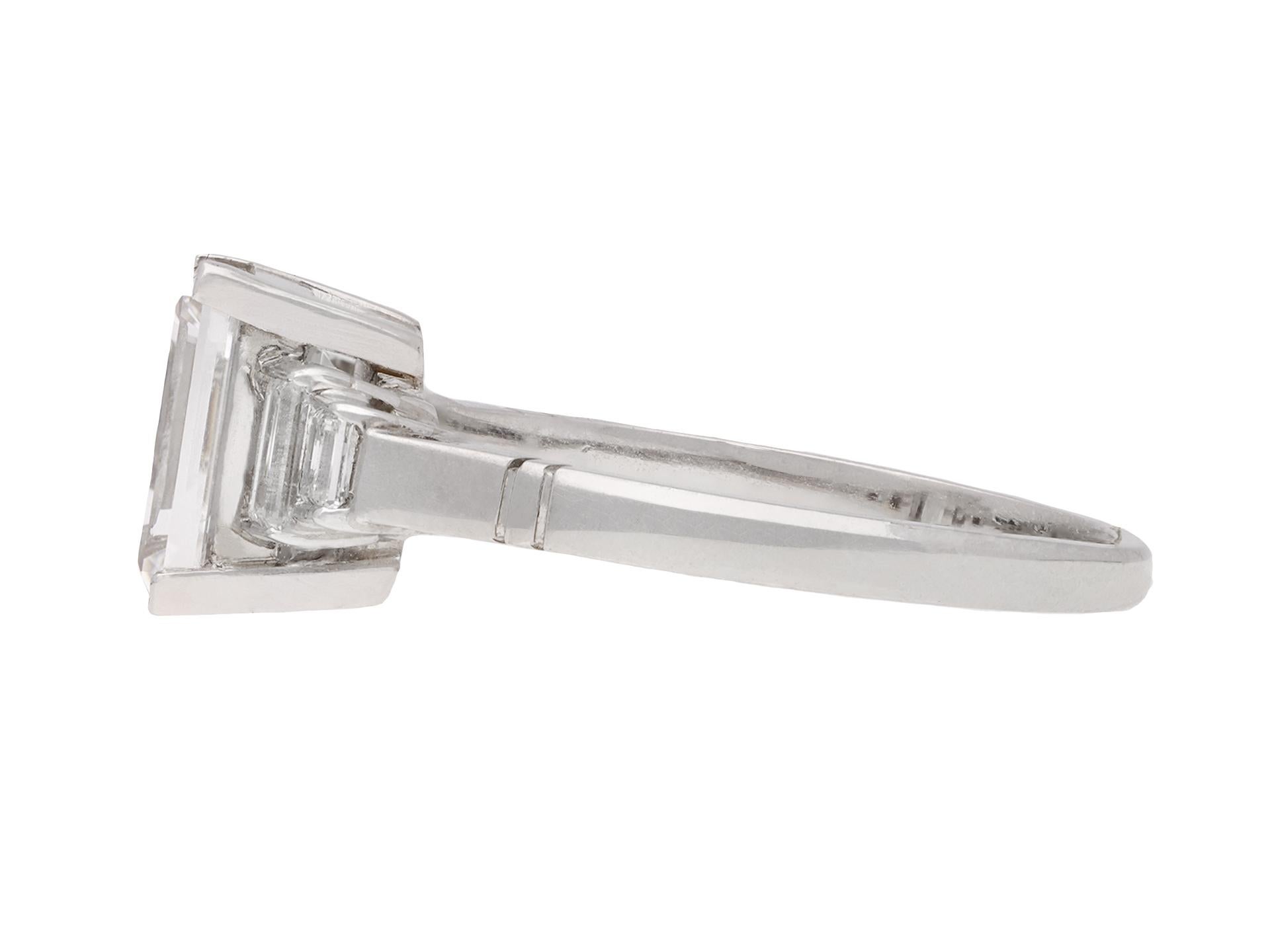 Art Deco step cut diamond ring. Set with one rectangular step cut diamond, E colour, VS2 clarity, with a weight of 2.07 carats in an open back claw setting, further set with four rectangular baguette cut diamonds in open back half rubover settings