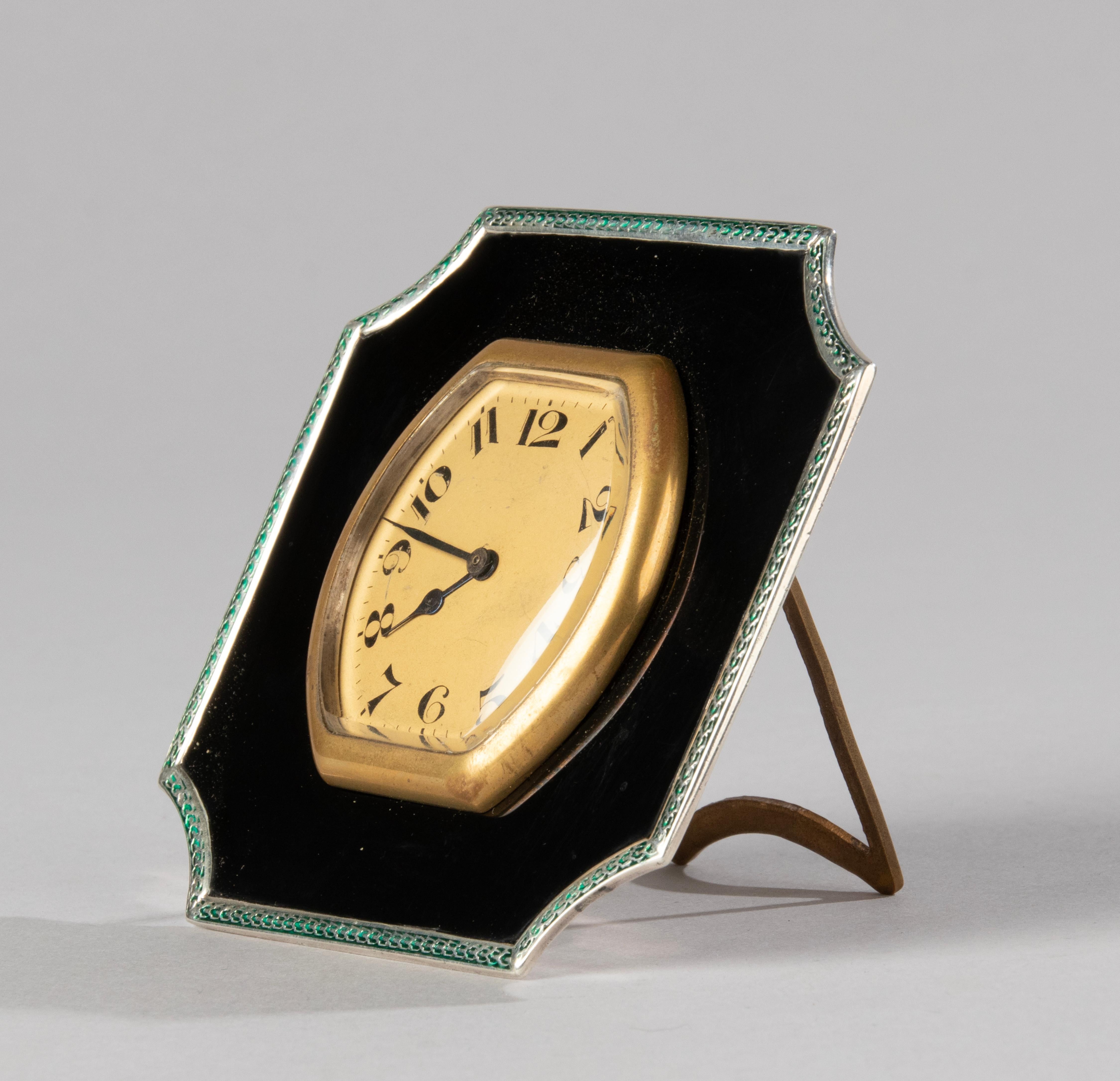 A lovely Art Deco table clock, made by the Birmingham silversmith Deakin and Francis, in 1928. 
The clockwork is of Swiss origin. The silver frame is very decorative with beautiful enamel work in green and black. The clock has a good mechanism, it