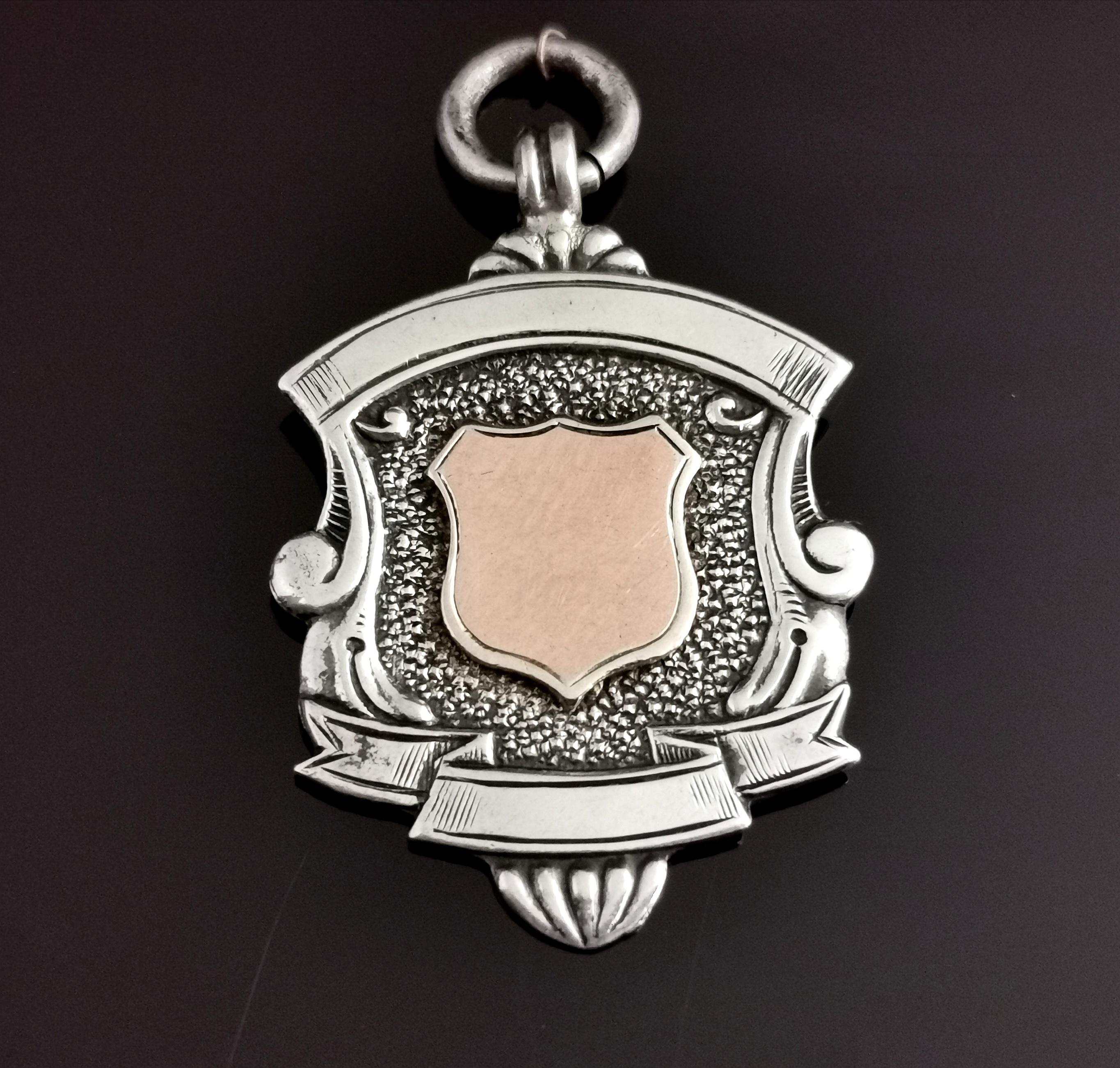 An attractive vintage, late 1920's sterling silver and Rose gold shield fob.

A nice attractive fob with a decorative design and a 9ct Rose gold shield shaped cartouche to the centre, this has not been monogrammed or engraved so could be