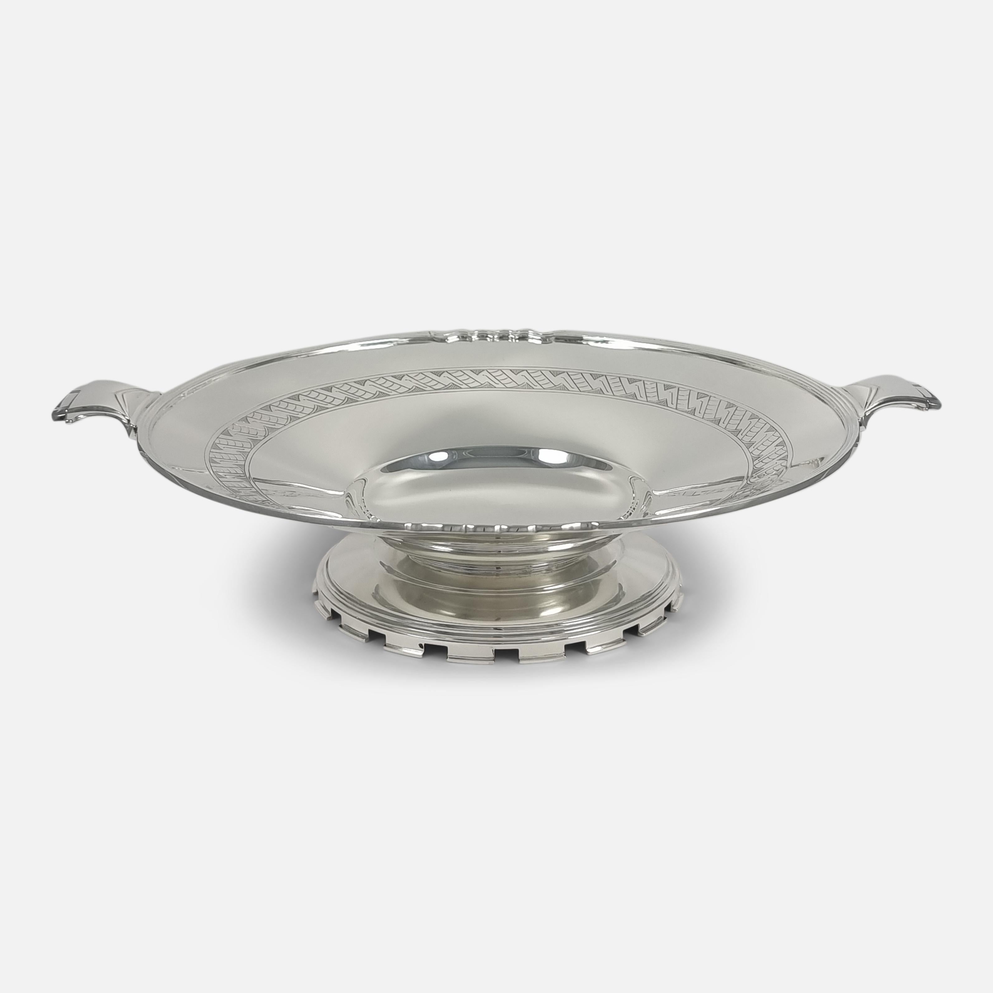 A Mappin & Webb sterling silver dish, designed in the Art Deco manner. This elegant dish features dual handles adorned with geometric patterns, a delicately reeded edge, and an intricately engraved inner band. It rests upon a distinctively