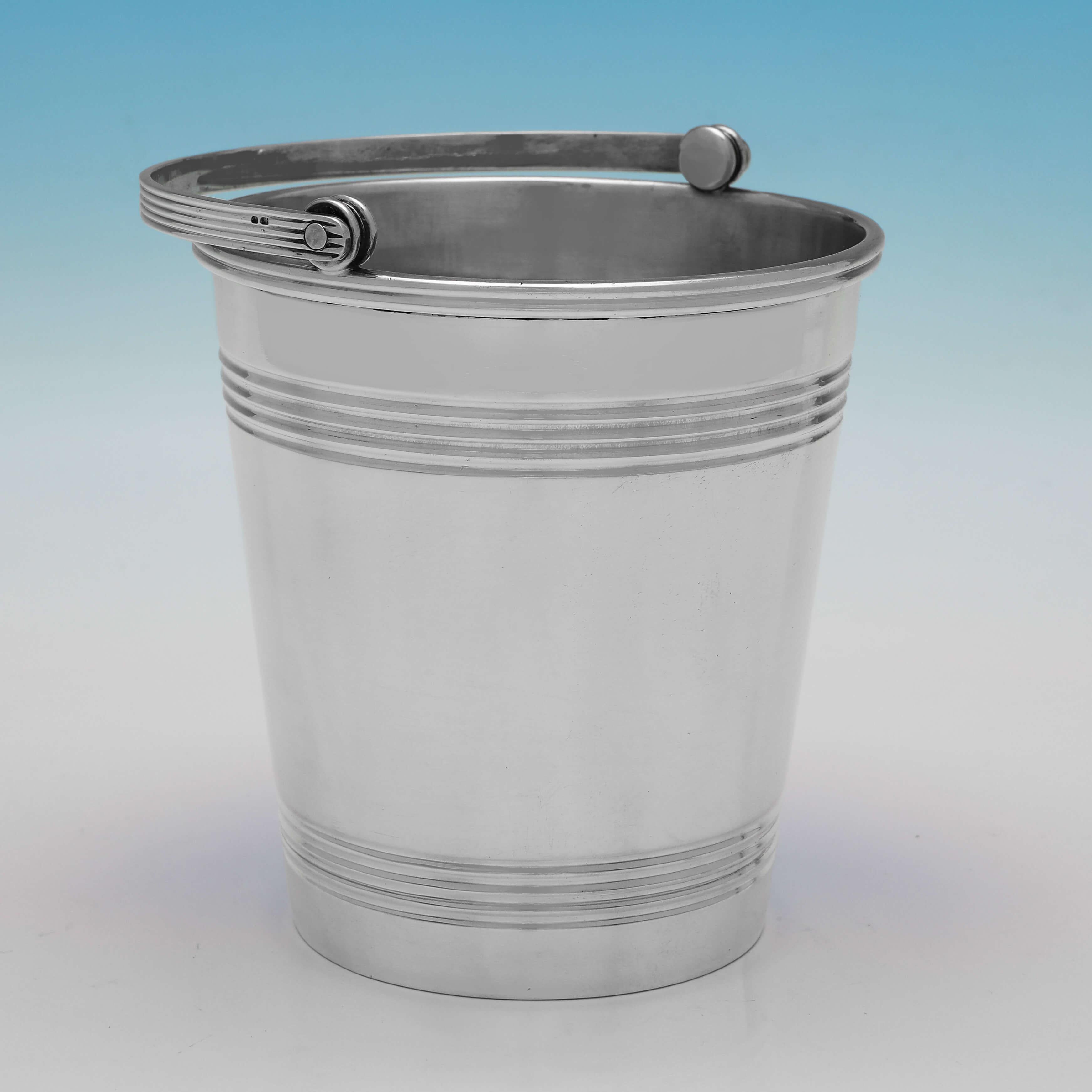 Hallmarked in London in 1937 by Goldsmiths & Silversmiths Co., this handsome, Sterling Silver Ice Bucket, is bucket shaped, featuring reed detailing, and a removable drainer. 

The ice bucket measures 5