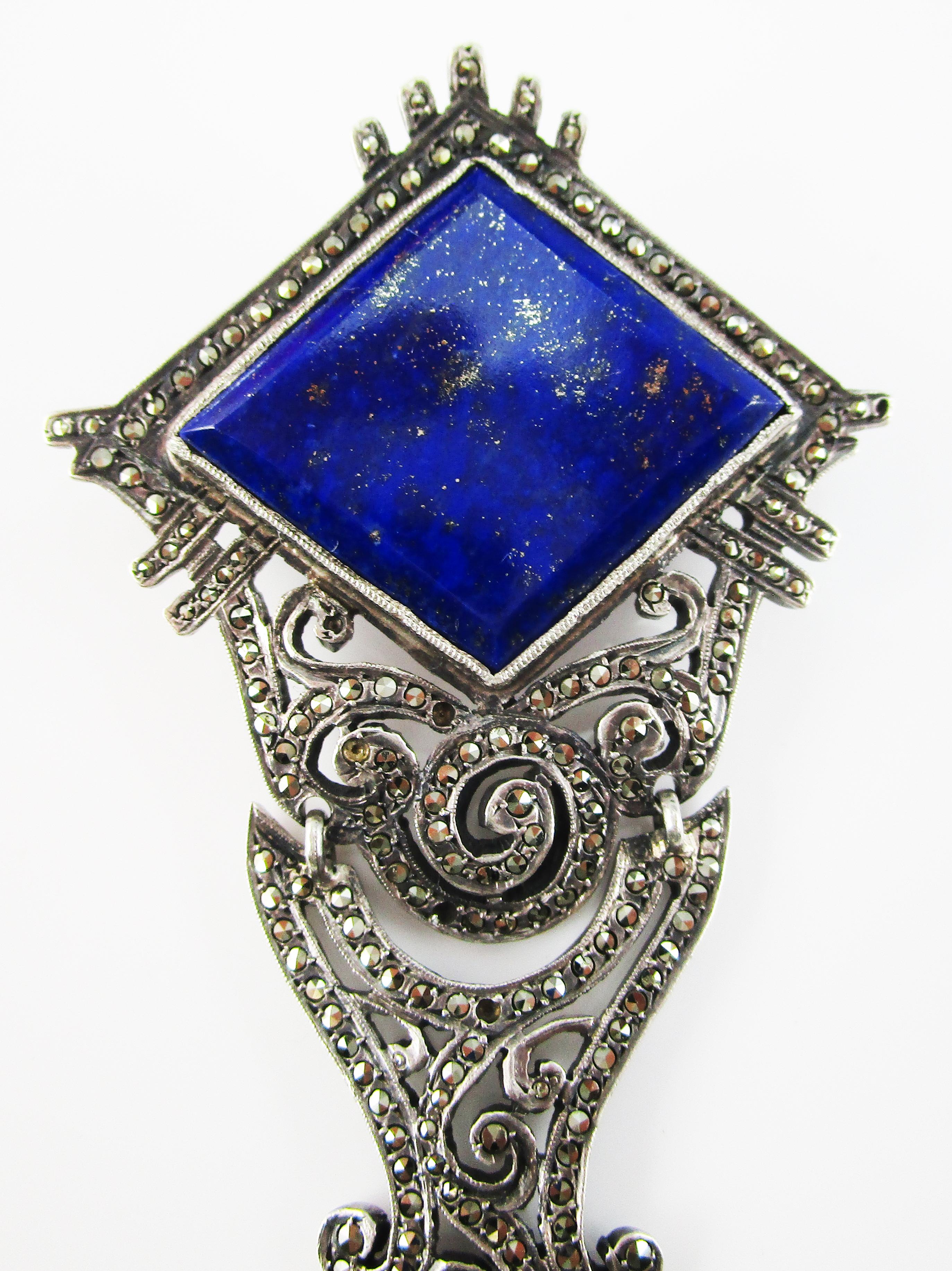 This is a gorgeous Art Deco pin in sterling silver featuring bright shiny marcasite, a stunning faceted natural blue lapis center, and a lovely peal dangle to finish it off! The pin features the strong lines and enchanting designs that are hallmarks