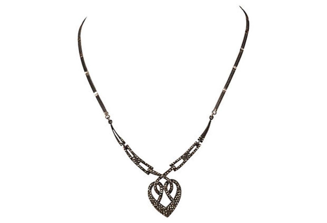 1940s sterling silver interwoven heart necklace pavé set with marcasites. Bib, 3 3/8”W. Heart pendant, 1”W x 1 3/8”H. Closes with jump ring and eye lit. Necklace was acid tested for sterling silver. Weighs, 15.3 grams.
