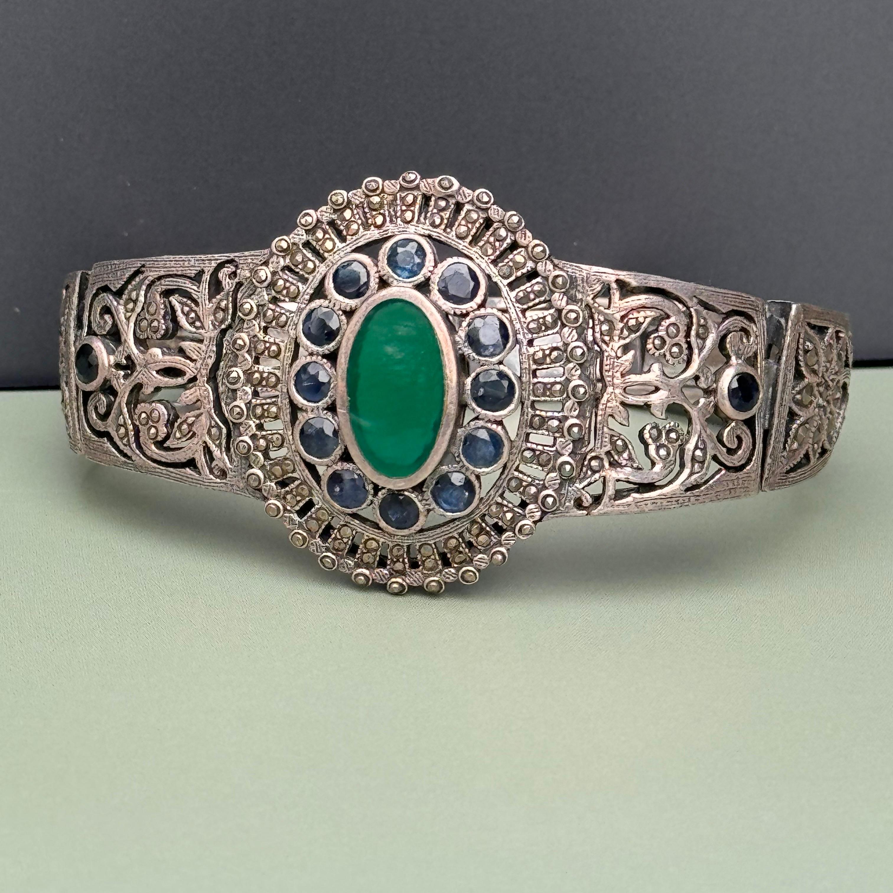 Vintage  Art Deco Sterling Silver Sapphire and Marcasite Bracelet  featuring a large central green onyx stone, radiating with rich color and elegance. Surrounding the onyx are 14 faceted genuine sapphire cabochons, each meticulously set to enhance