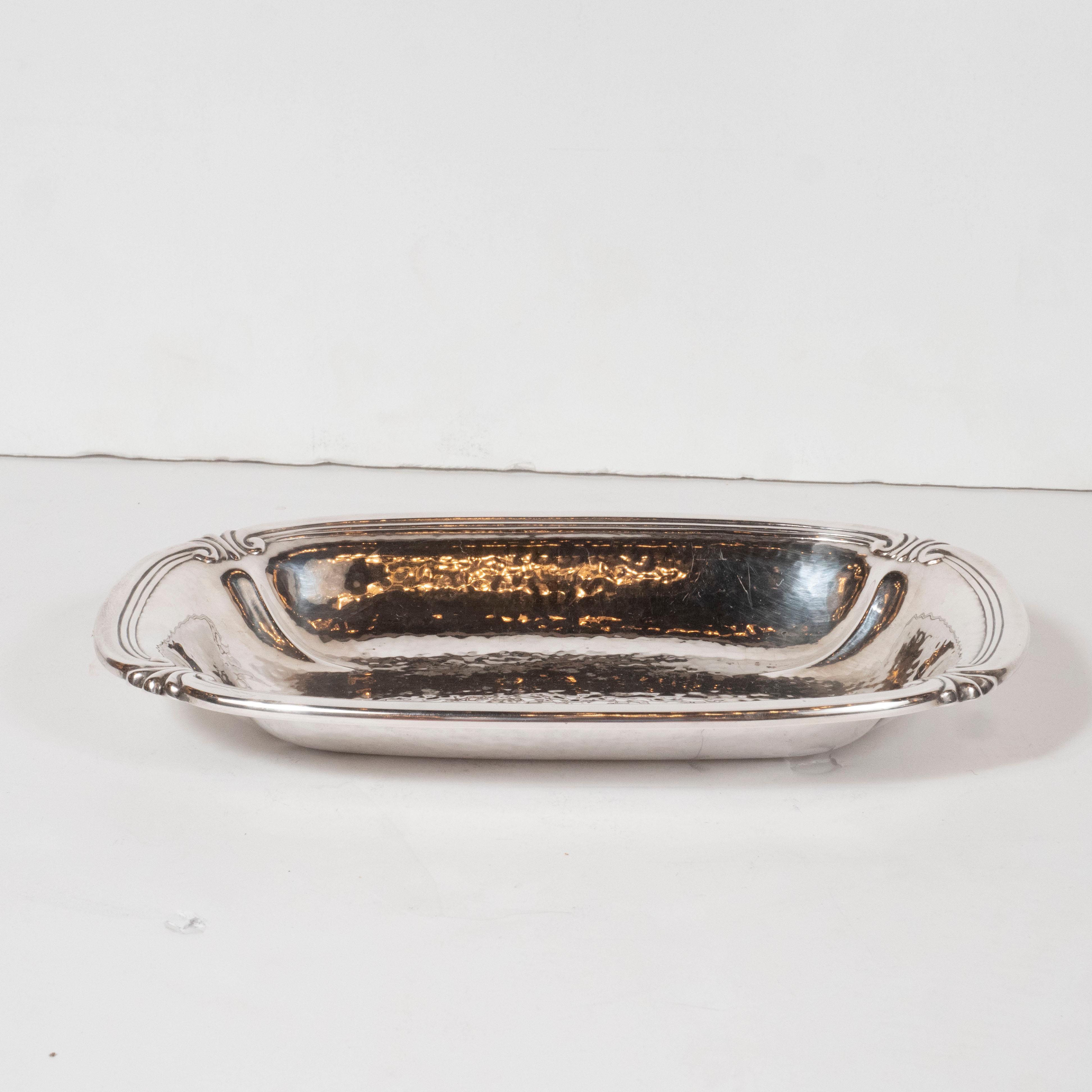 This elegant Art Deco tray was realized by the esteemed International Silver Company in the United States circa 1930. It features an oval form with raised sides adorned with channel detailing and neoclassical stylized motifs at each corner. With