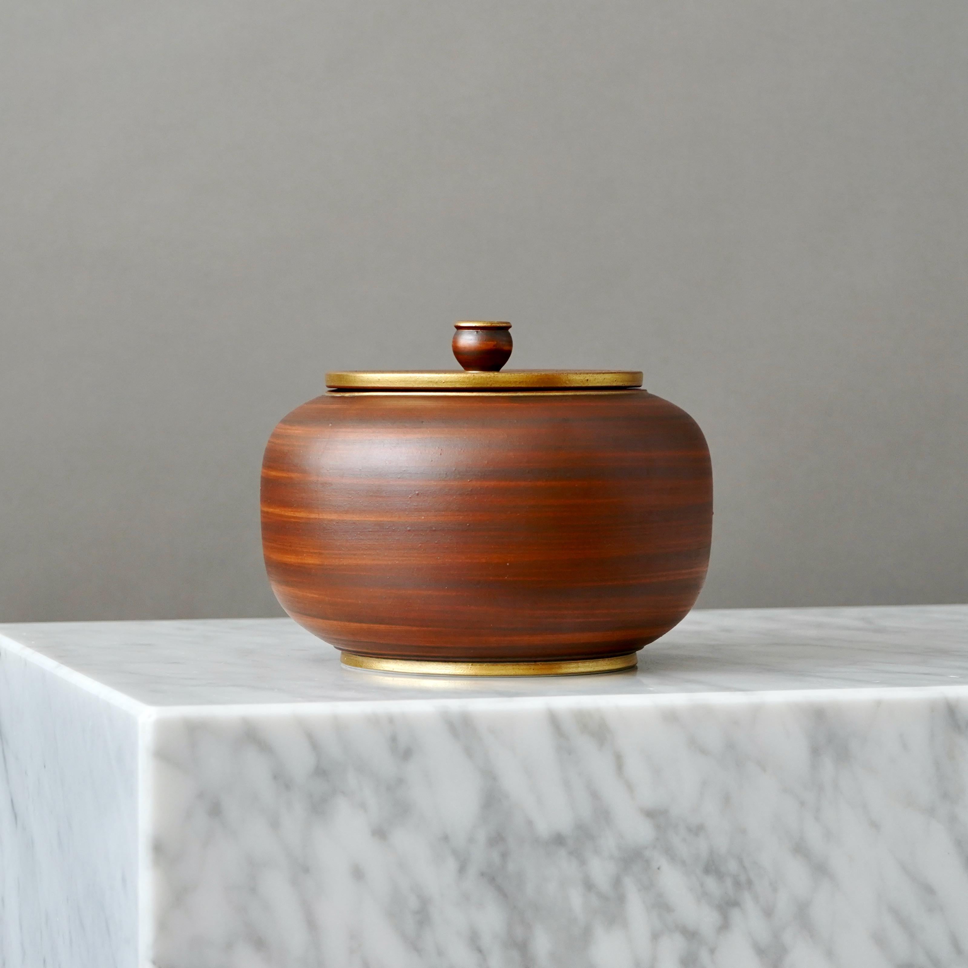 A stoneware art deco lidded bowl with beautiful brown glaze. Foot and mouth detailed in gold.
Designed by Gunnar Nylund for ALP (Lidköpings Porslinsfabrik), Sweden, 1930s.

Great condition.
Stamped 'ALP', 'Modell Nylund', 'Lidköping, SWEDEN' and