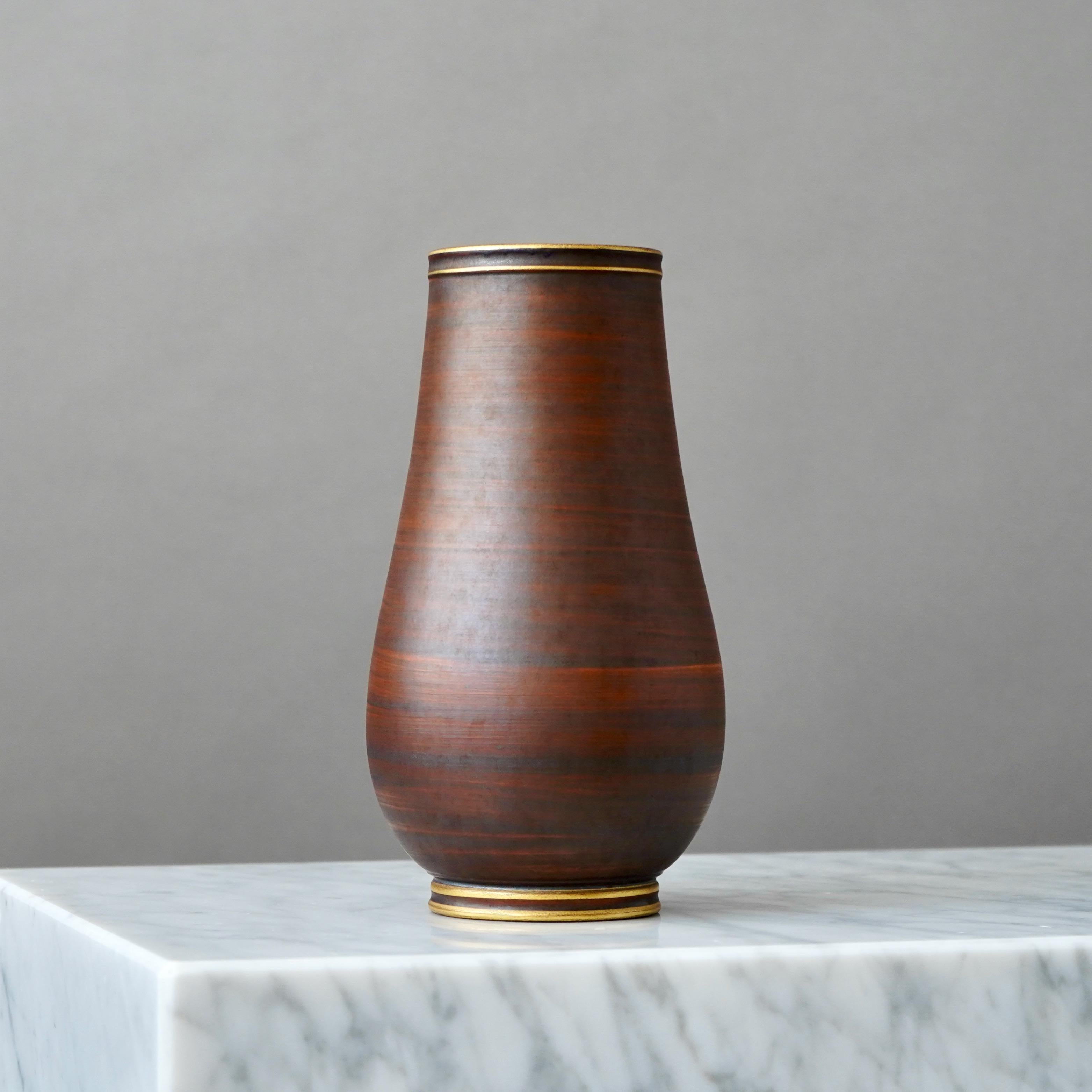 A stoneware art deco vase with beautiful brown glaze. Foot and mouth detailed in gold.
Designed by Gunnar Nylund for ALP (Lidköpings Porslinsfabrik), Sweden, 1930s.

Great condition, only some slight wear to the gold. 
Stamped 'ALP', 'Modell