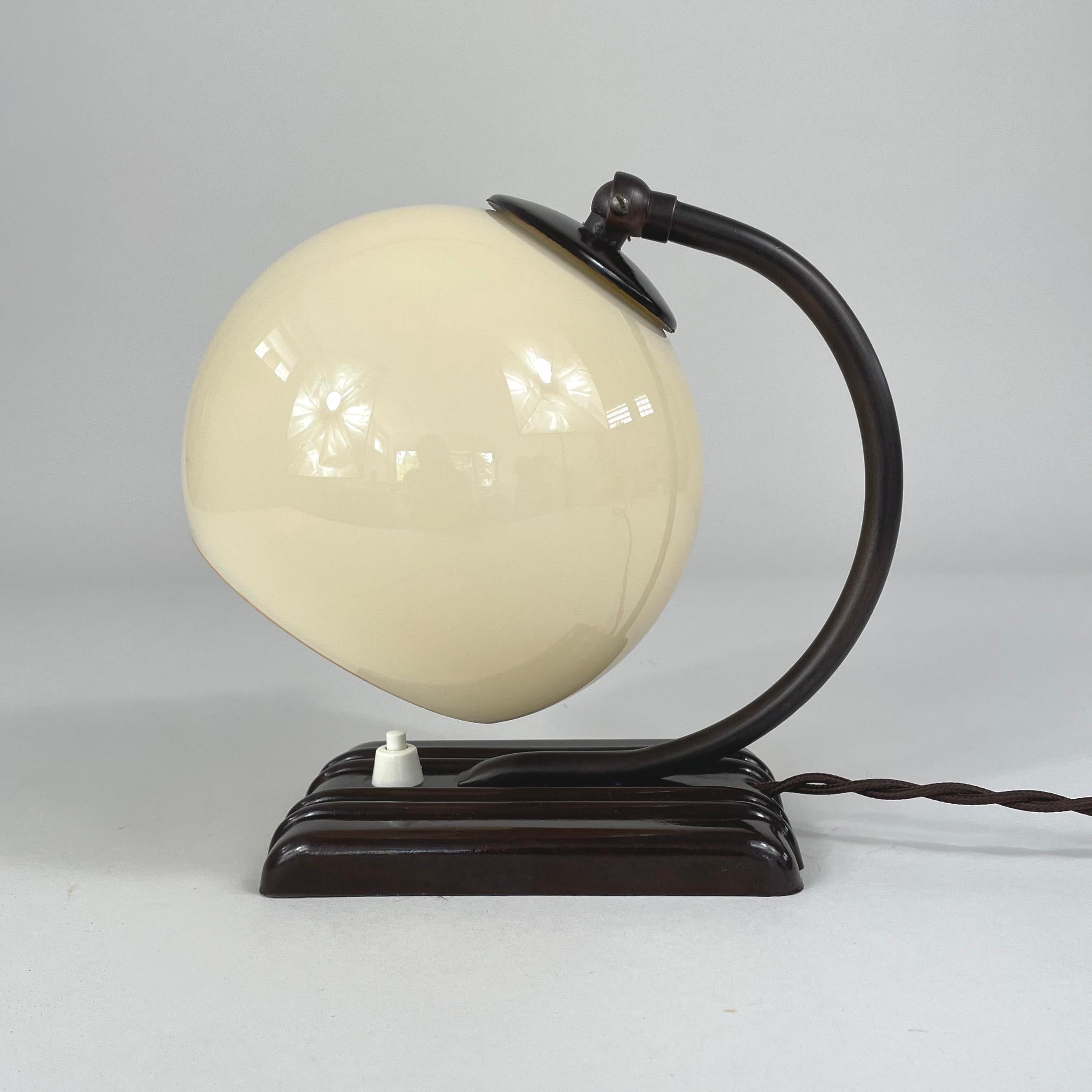 This unusual vintage table or bedside lamp was designed and manufactured in Germany in the 1920s-1930s during the Bauhaus period. It is made of bronzed brass, has got an adjustable lamp shade in ivory colored opaline glass and a dark brown shiny