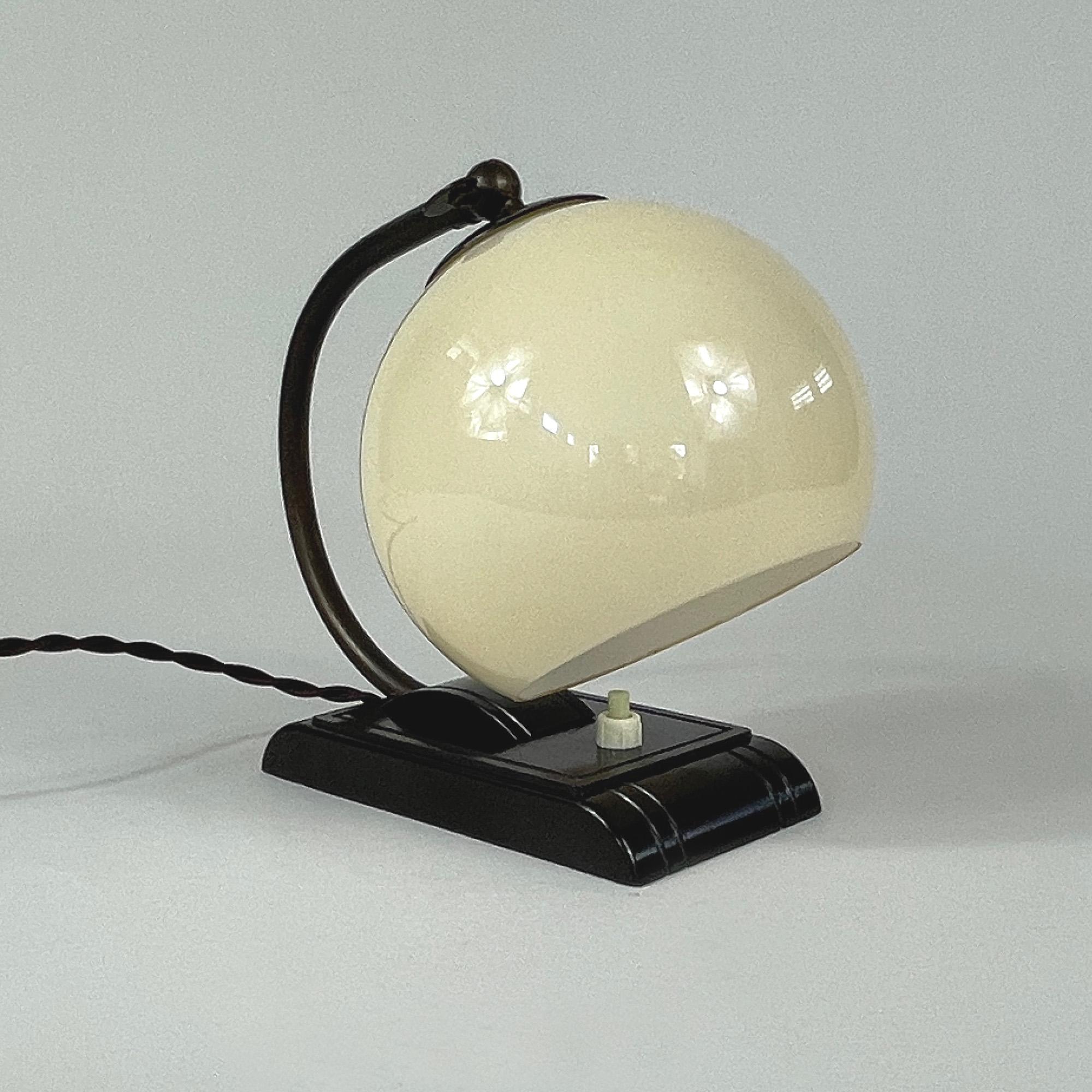 This unusual vintage table or bedside lamp was designed and manufactured in Germany in the 1920s-1930s during the Bauhaus period. It is made of bronzed brass, has got an adjustable lamp shade in ivory colored opaline glass and a dark brown shiny