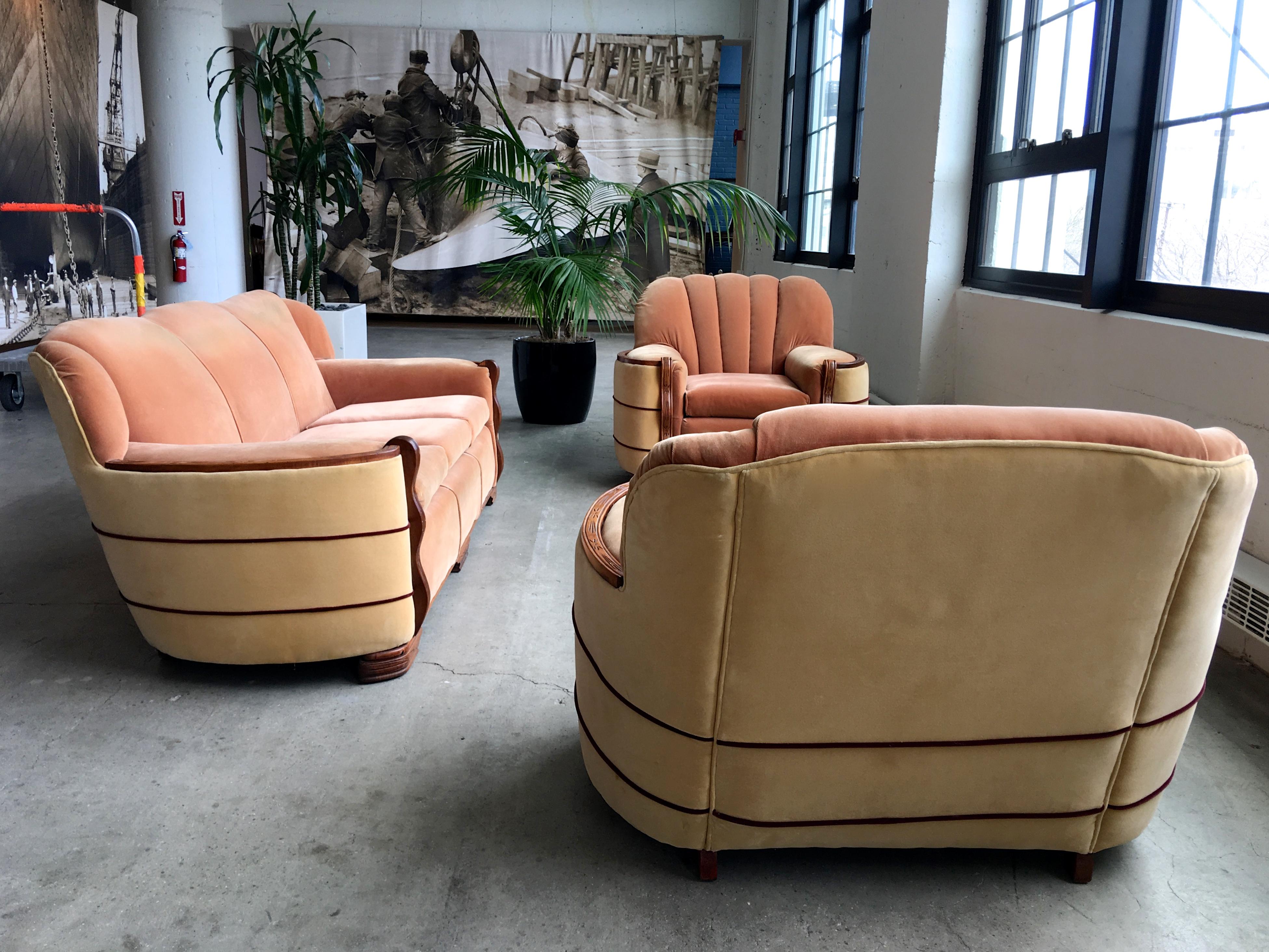 Authentic Art Deco seating suite including a 3-seat sofa and pair of club chairs upholstered in two-tone apricot and beige/peach mohair. Top and front of arms are trimmed in carved walnut, the vertical fronts having undulating wave-like form, a