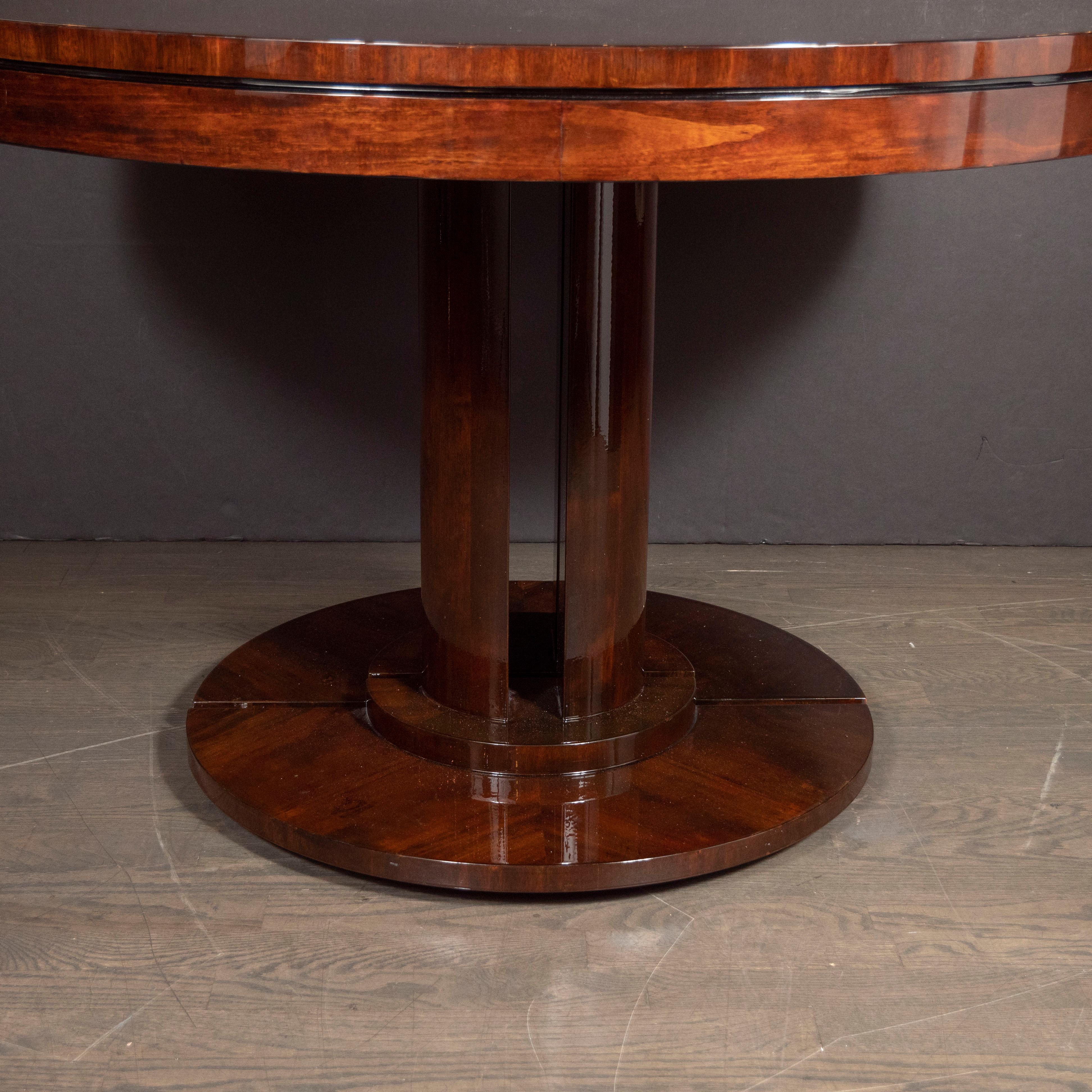 This elegant and stately Art Deco dining/ center table was realized in the United States, circa 1930. It features a circular base and top executed in beautiful walnut with streamlined supports. Two leaves accompany the table, allowing it to be