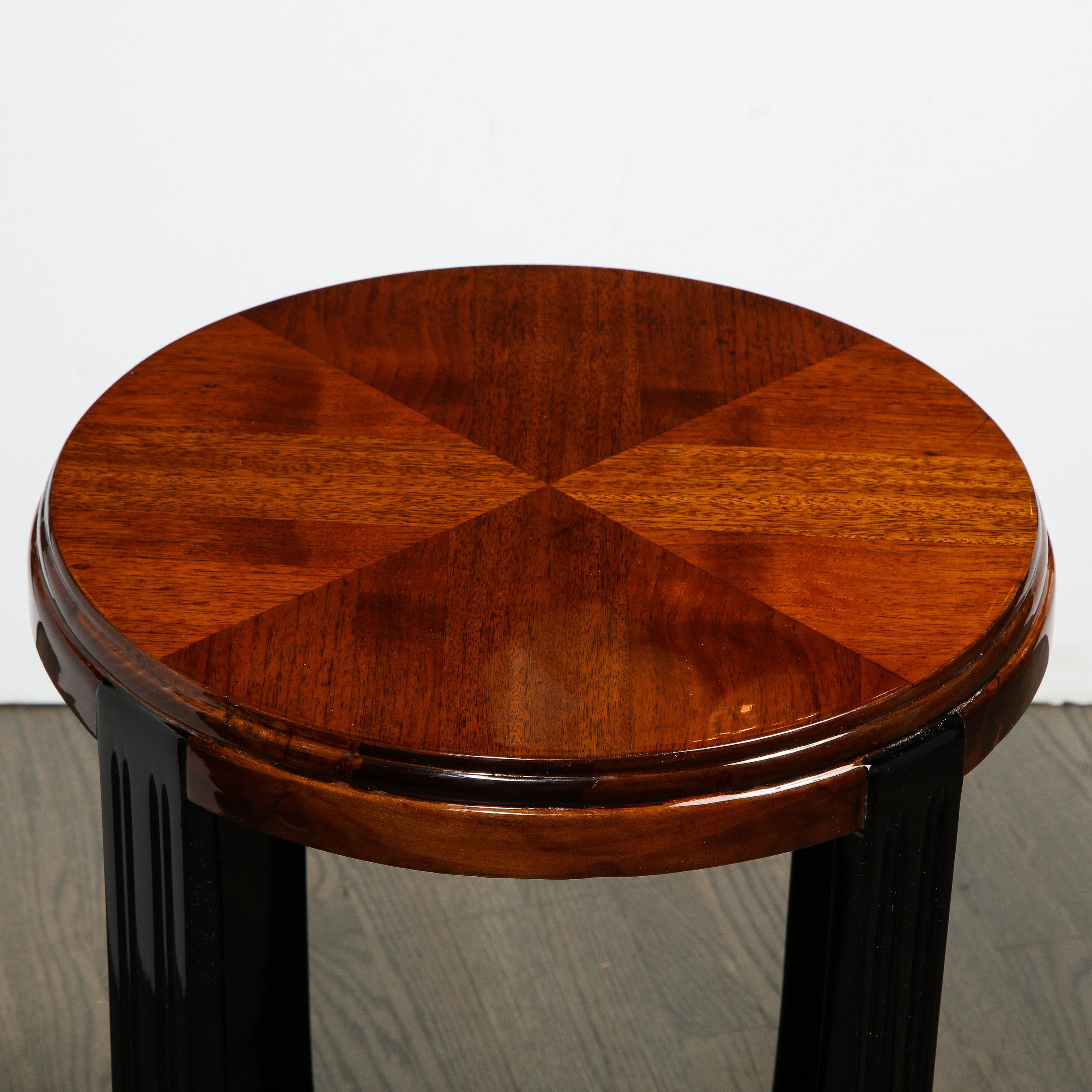 This beautiful Art Deco Machine Age table was realized in the United States circa 1935. It features a round top with geometric marquetry in bookmatched walnut; black lacquer streamlined supports; and an X-form base in walnut with streamlined