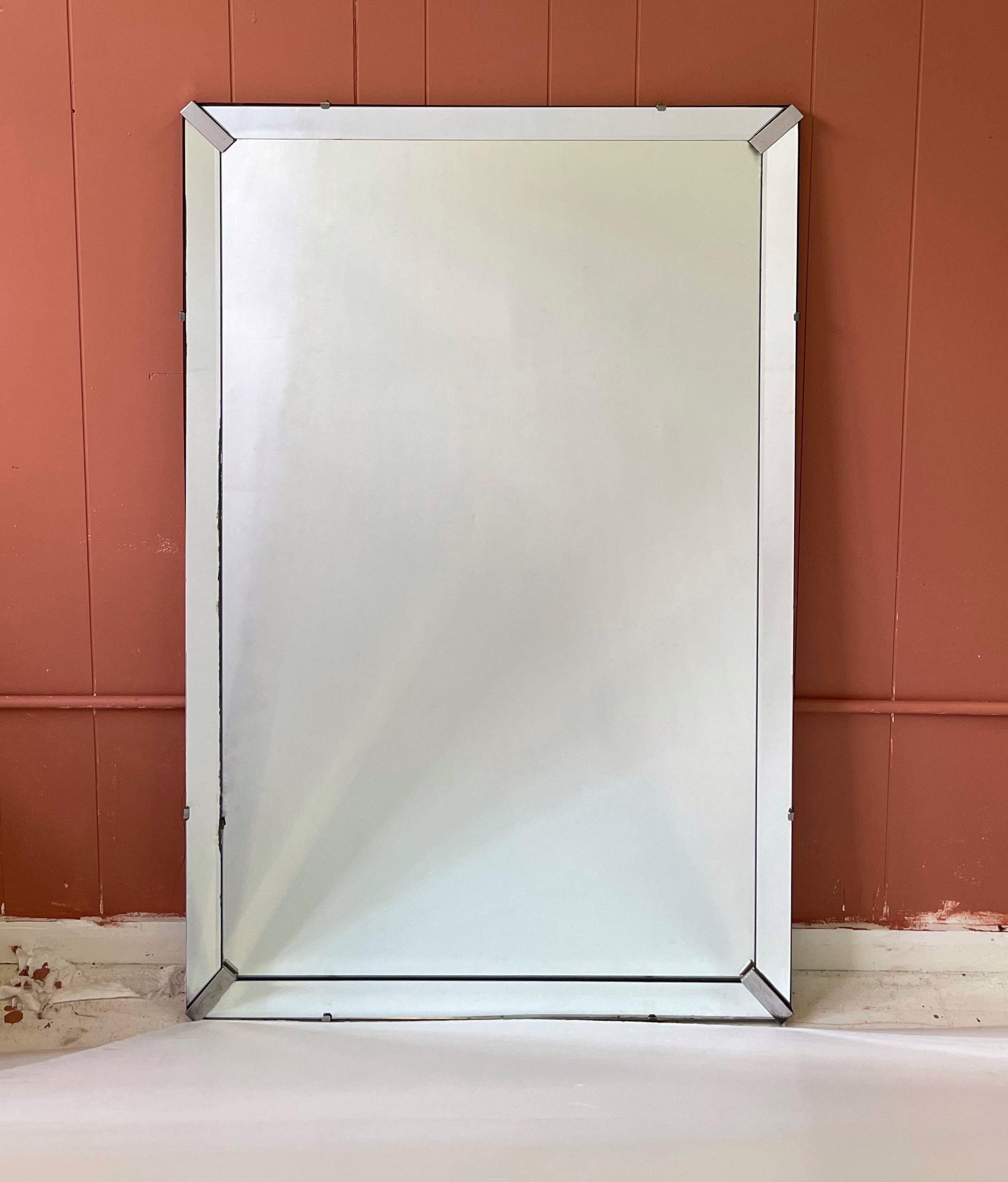 Large scale streamlined 1940's Art Deco wall mirror held in a beveled mirror frame with nickel fittings.
