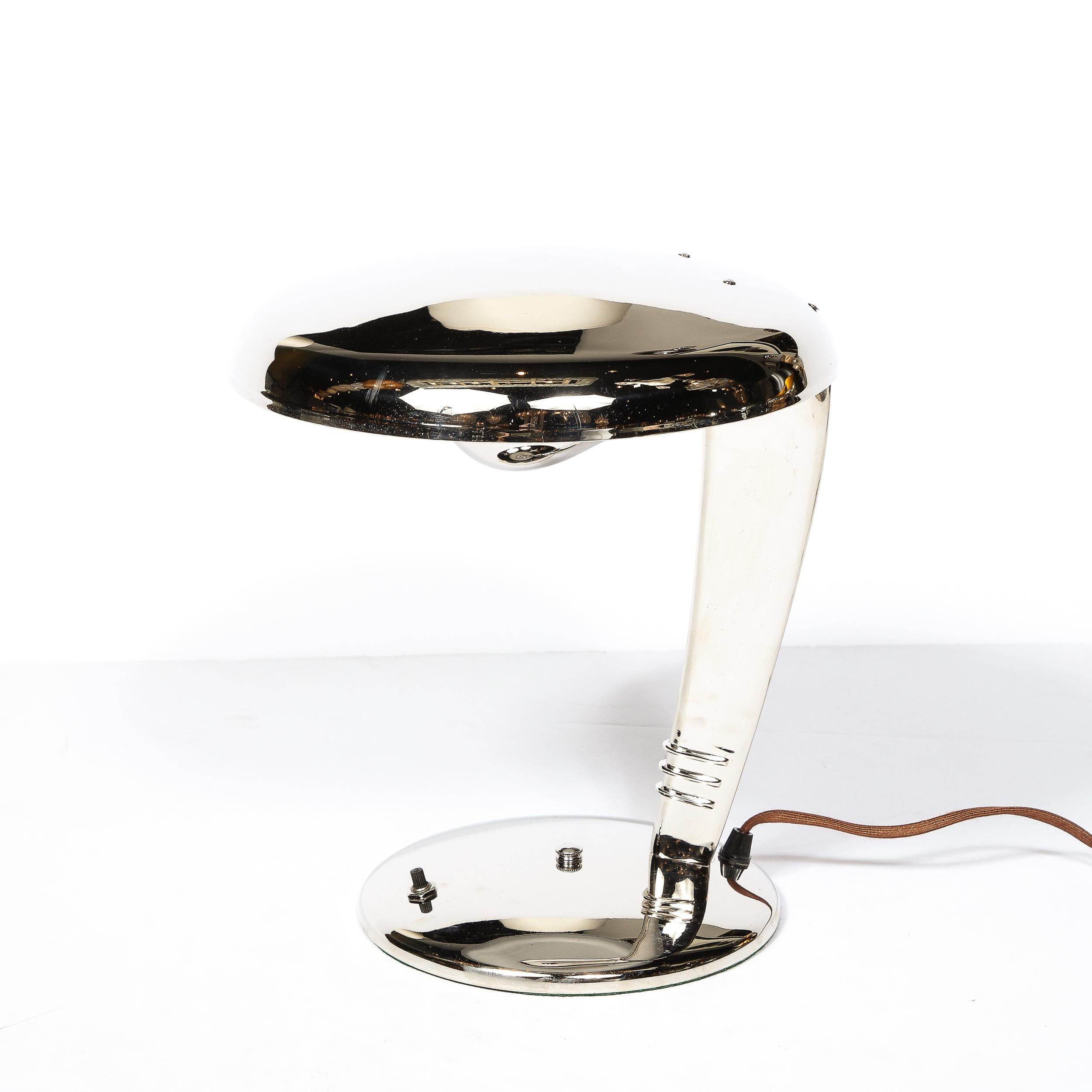 This Art Deco Cobra Table lamp originates from the United States Circa 1930 designed by Norman Bel Geddes for Fairies. A handsome example of Art Deco design and material beauty, this piece features a streamlined profile in Polished nickle with a