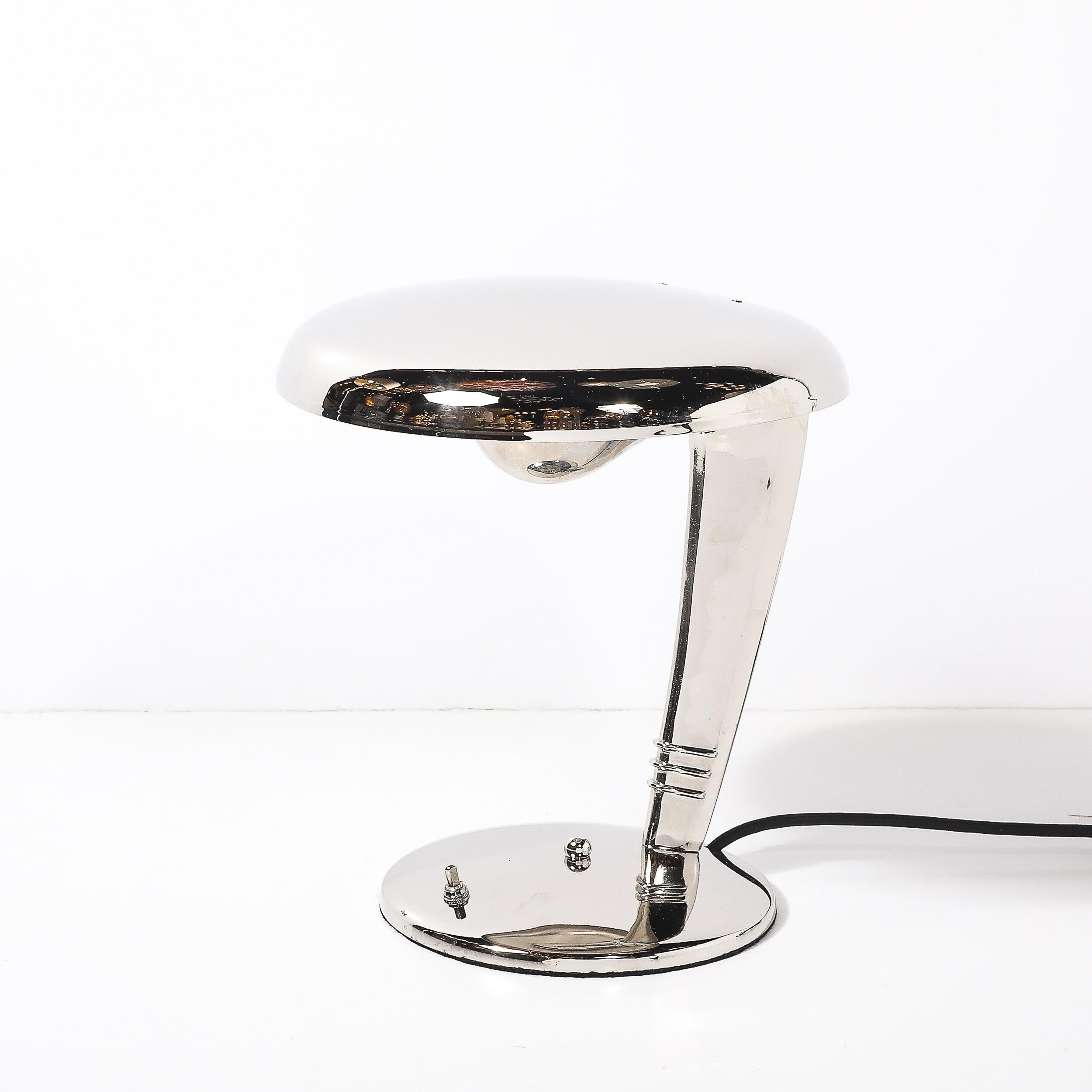 This Art Deco Cobra Table lamp originates from the United States Circa 1930 designed by Norman Bel Geddes for Fairies. A handsome example of Art Deco design and material beauty, this piece features a streamlined profile in Polished nickle with a