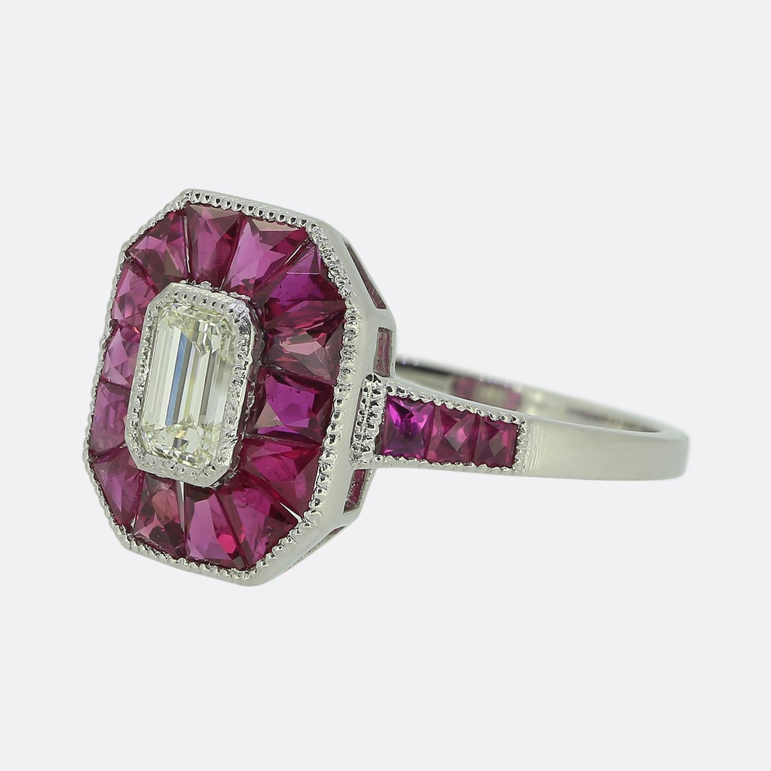 Here we have an 18ct white gold diamond and ruby ring. At the centre of the face we find a 0.45 carat emerald cut diamond surrounded by an array of perfectly matched calibre cut pinky red rubies which continue onto either shoulder. The ring is of an