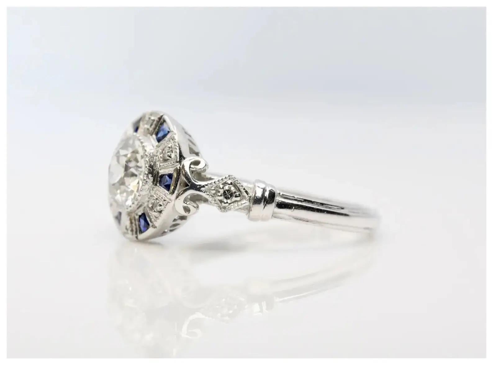 A handmade Art Deco style diamond target form engagement ring in platinum.

Centered by a 0.71 carat old European cut diamond set in a miligrained platinum bezel.

Framed by six French cut blue sapphires of 0.18ctw and eight pave set diamonds of