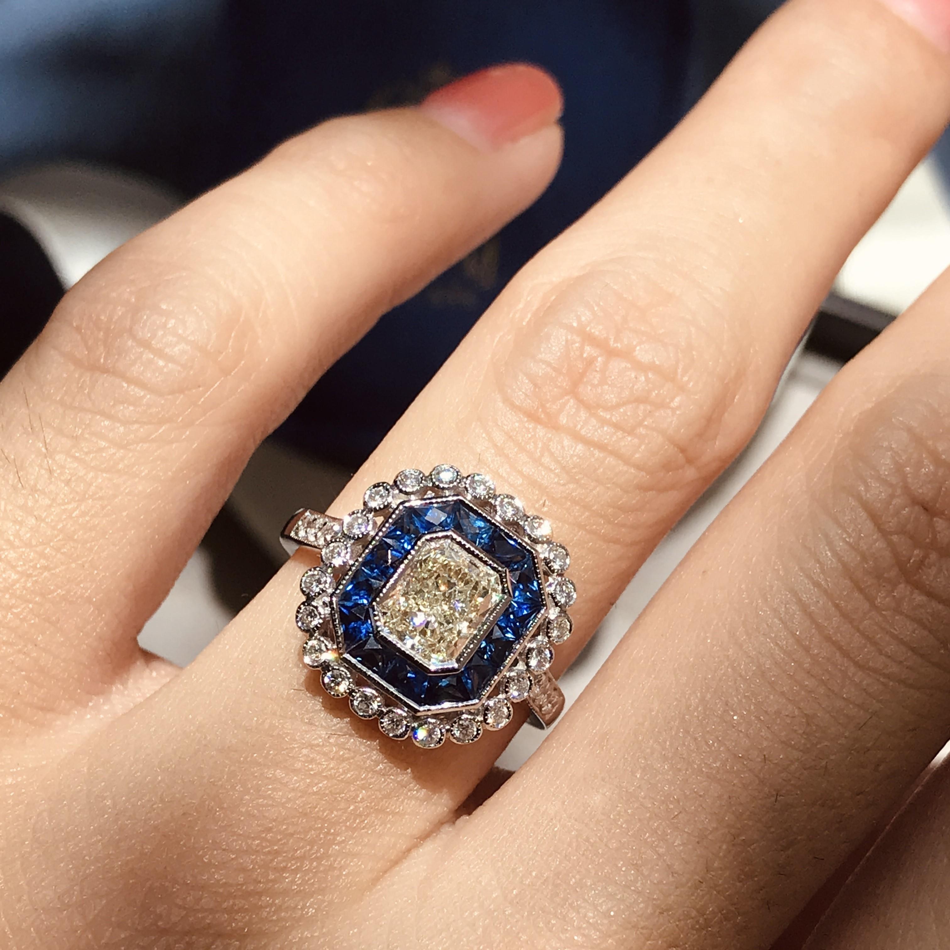 An 18k white gold Art-Deco design diamond and sapphire target ring, center K/VS diamond with an outer ring of round diamonds an inner one of French cut sapphires and finished with millgrain edging, finished with diamond shoulders.

Ring