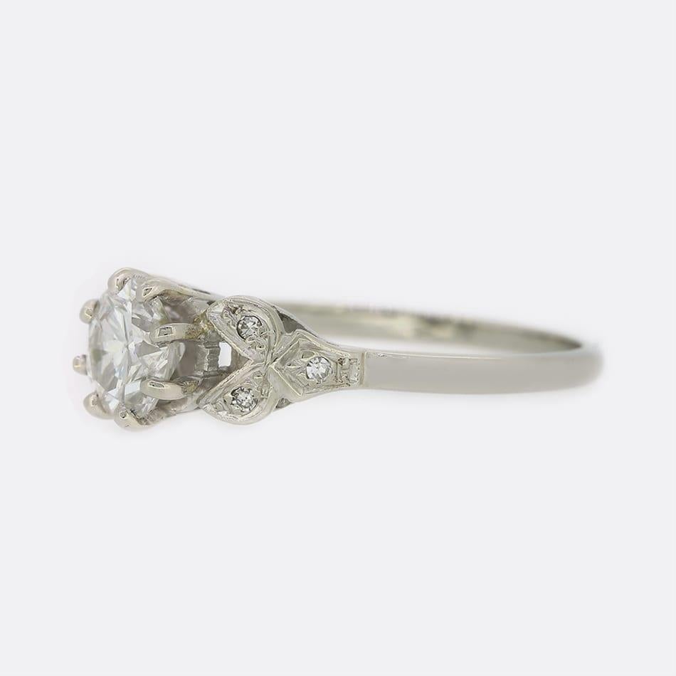 This is an Art deco style platinum and diamond engagement ring. The ring plays host to a 1.05 carat old cut diamond set in a raised 8 clawed mount. The shoulders of the ring are a lovely foliate design and each feature 3 single cut