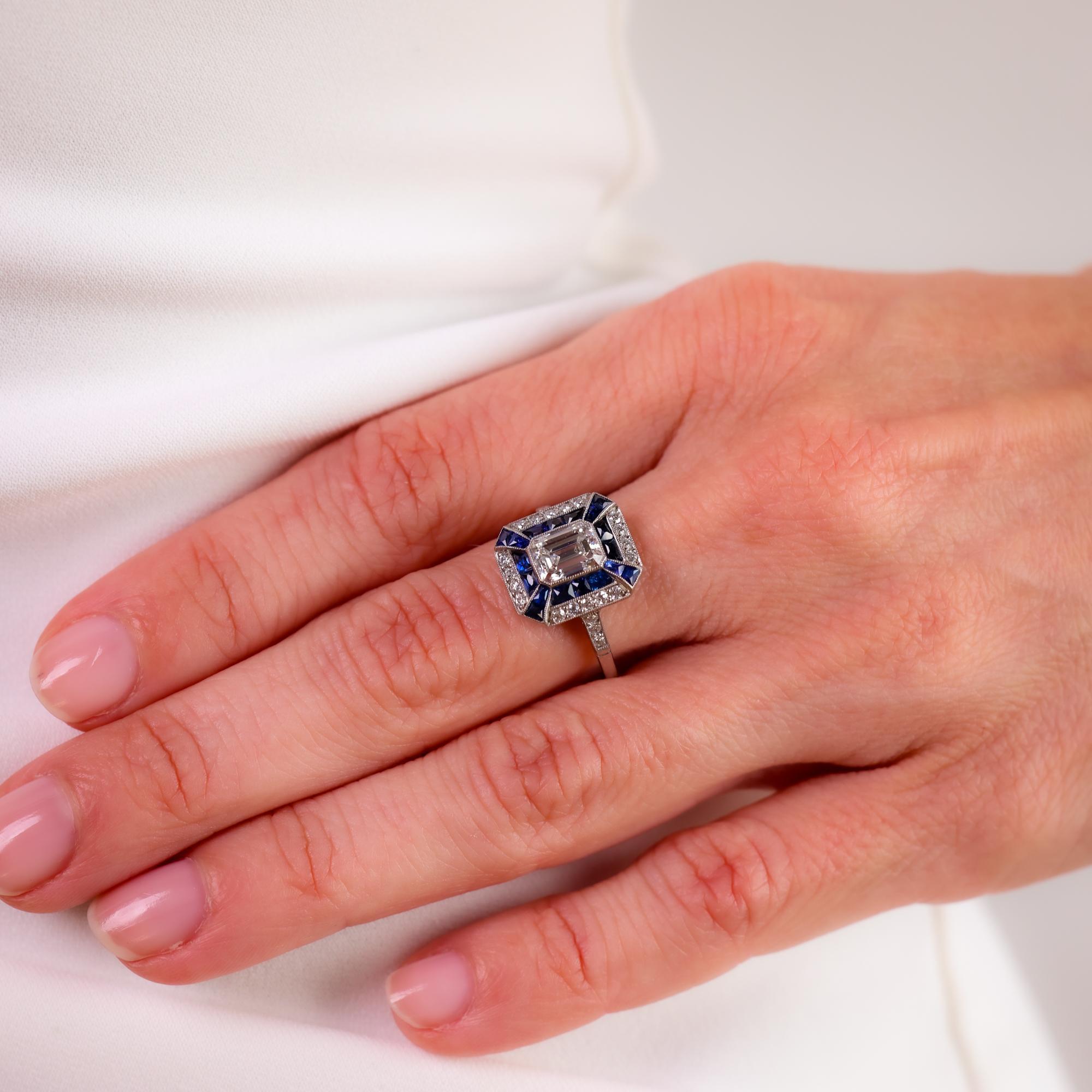 Este anillo de platino de estilo Art Decó de los años 90 exhibe un llamativo diamante talla esmeralda de 1,06 quilates, enmarcado por diamantes talla vieja europea y zafiros talla calibre azul profundo para una elegancia vintage atemporal.

Piedra