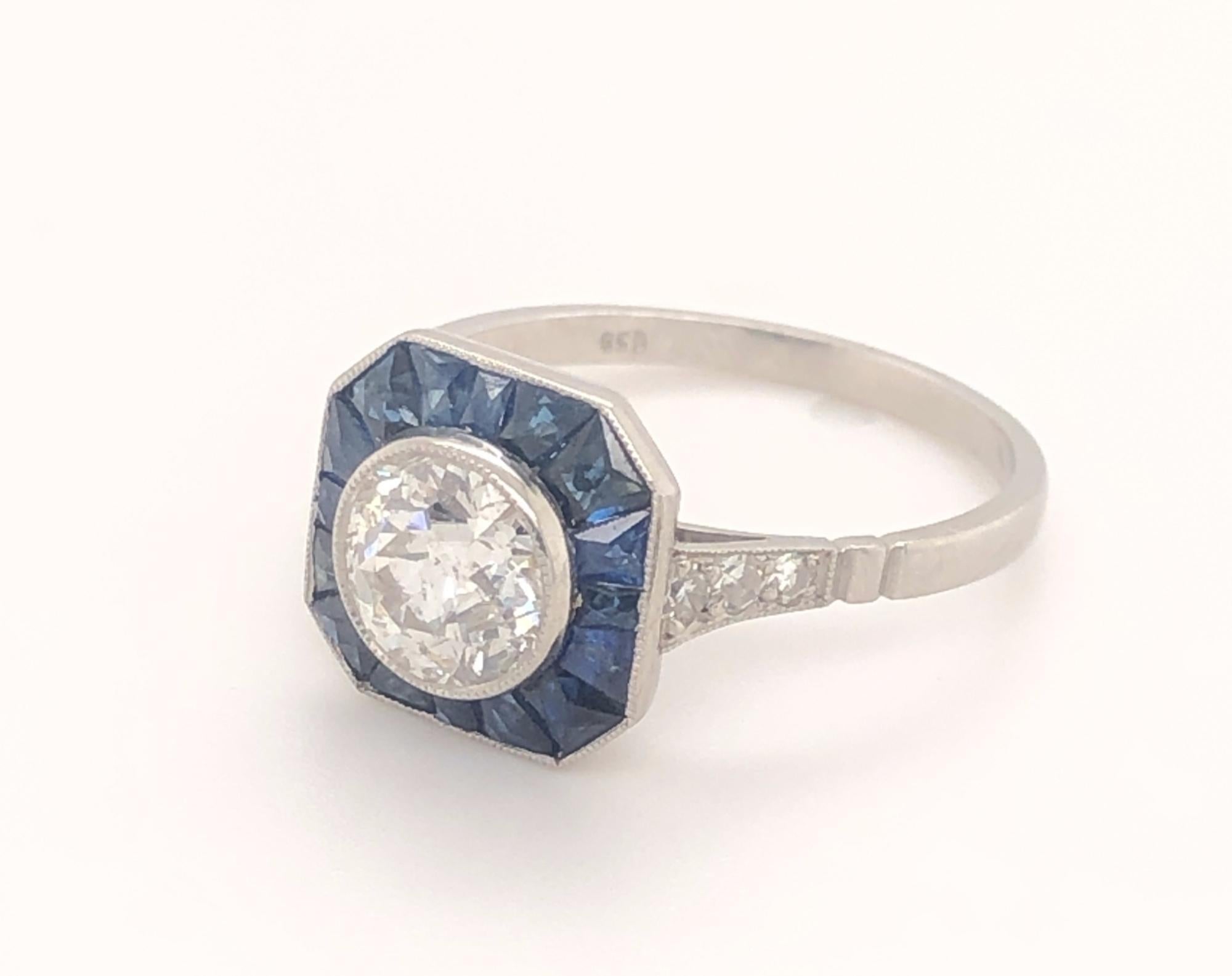 Art Deco Style 1.1 Euro Cut Diamond Sapphires Platinum Engagement Ring. This is a stunning art deco style engagement ring set with 1.18 round European cut diamond with a halo of natural sapphires set in platinum. Each shoulder has three round