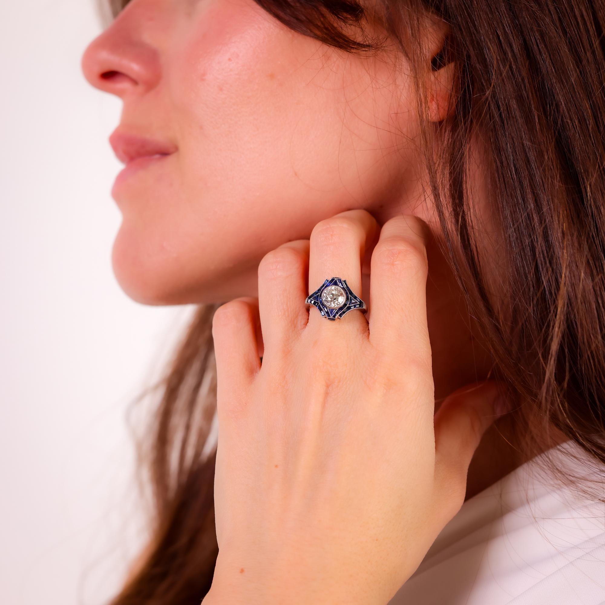 Cette bague moderne en platine de style Art déco met en valeur un diamant de taille européenne ancienne de 1,31 carat, entouré de saphirs de calibre vibrant de 1,50 carat, pour un design intemporel.

Pierre centrale : Diamant de taille européenne