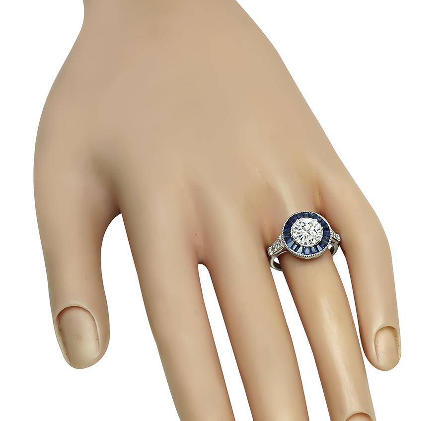 This is a fabulous 18k white gold halo engagement ring. The ring is centered with sparkling round cut diamond that weighs approximately 1.42ct. The color of the diamond is G-H with SI3 clarity. The center diamond is accentuated by sapphire and