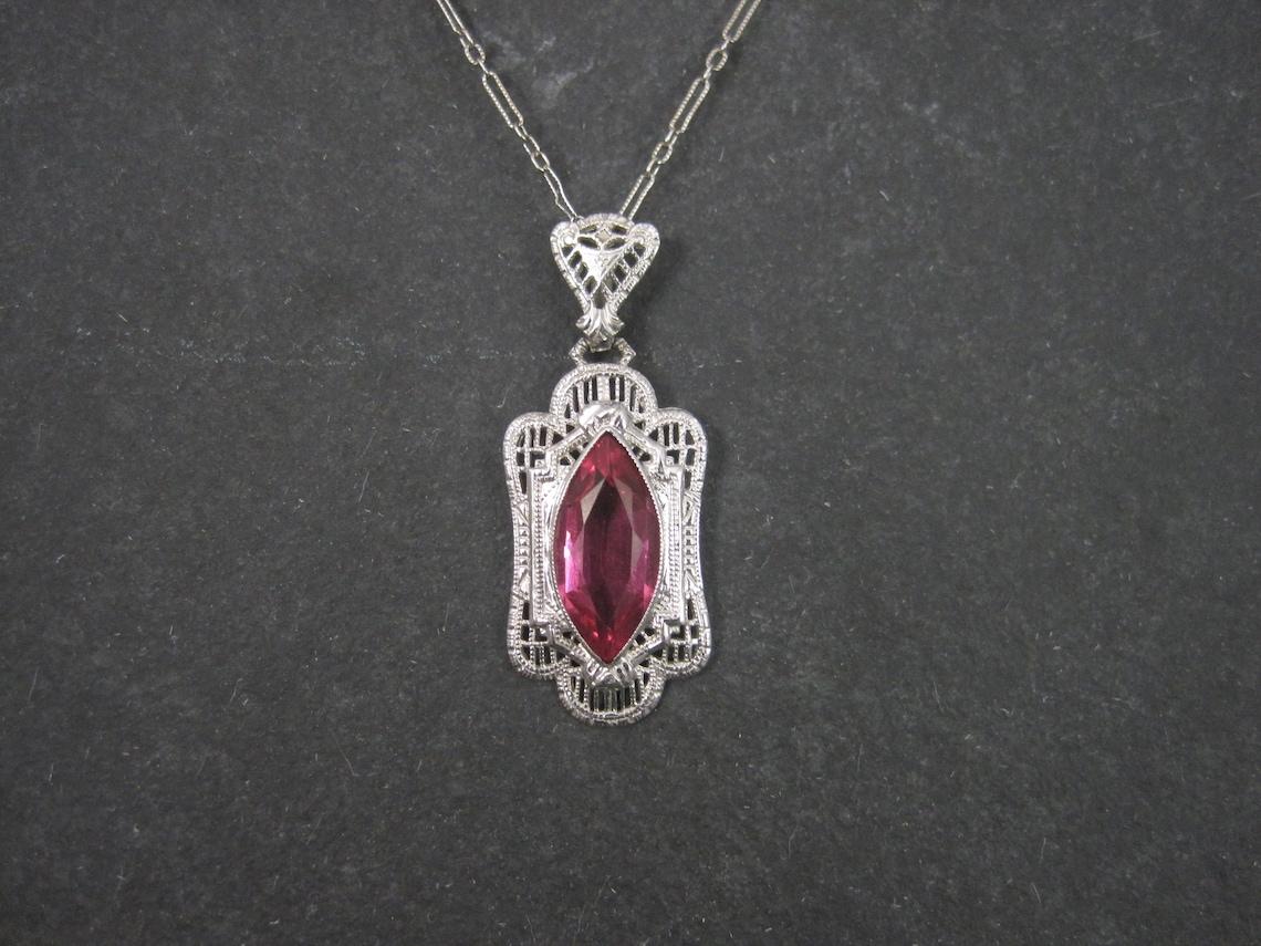 This beautiful vintage pendant is a late 80s to early 90s reproduction from an original Art Deco wax cast.
It is 14k white gold with simulated pink sapphire.

The pendant measures 9/16 by 1 5/16 inches
Marks: 14K

The pendant comes on a dainty 14k