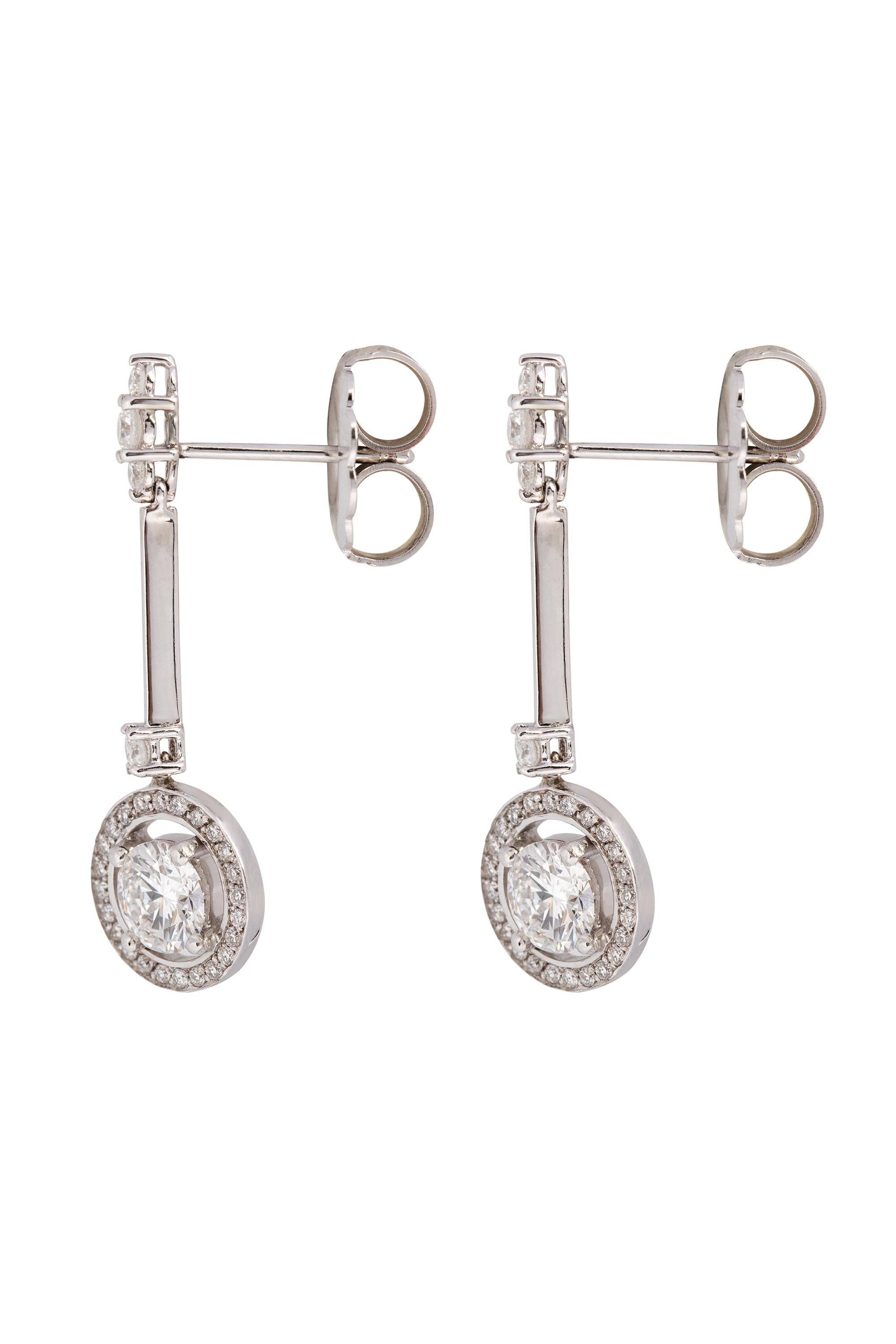 A beautiful pair of Art Deco inspired diamond drop earrings mounted in 18-karat white gold. These chic dangles feature two bright white round brilliant diamonds, E-F in color, VS in clarity with an approximate total weight of 1 carat, centered