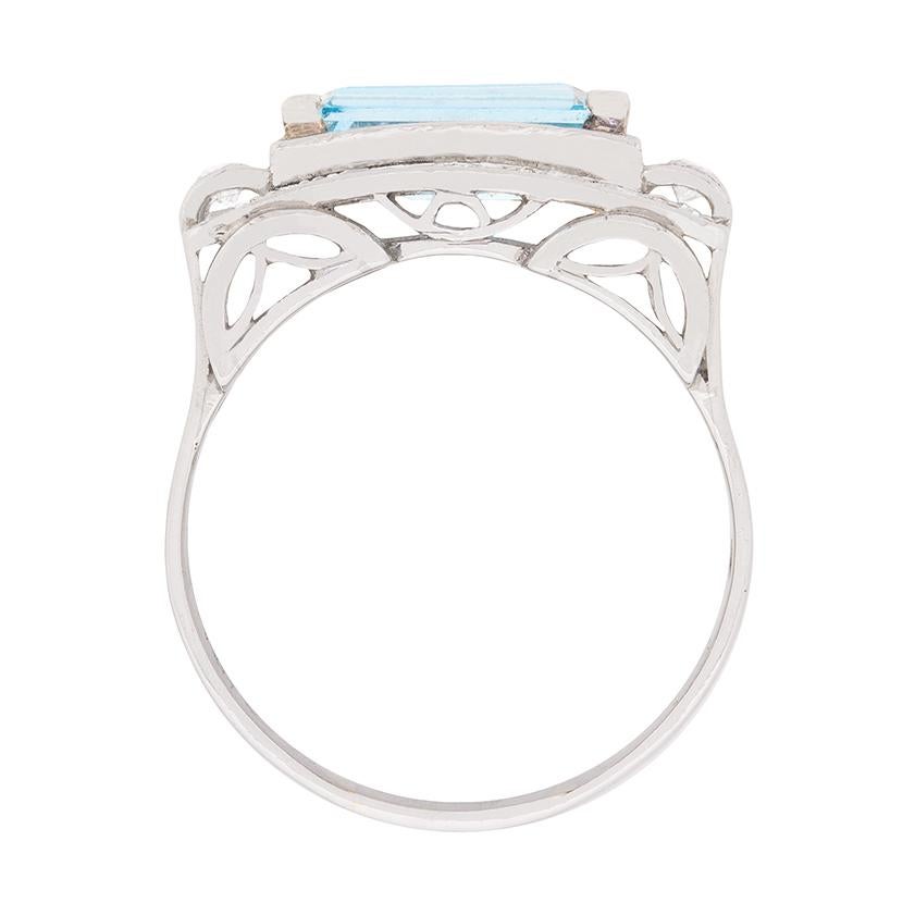 This 1940s aquamarine and diamond cluster cocktail ring harkens back to the opulent geometric designs of the Jazz Age! Set horizontally at its centre with a 1.50 carat swimming pool blue emerald cut aquamarine, this Art Deco style ring scintillates