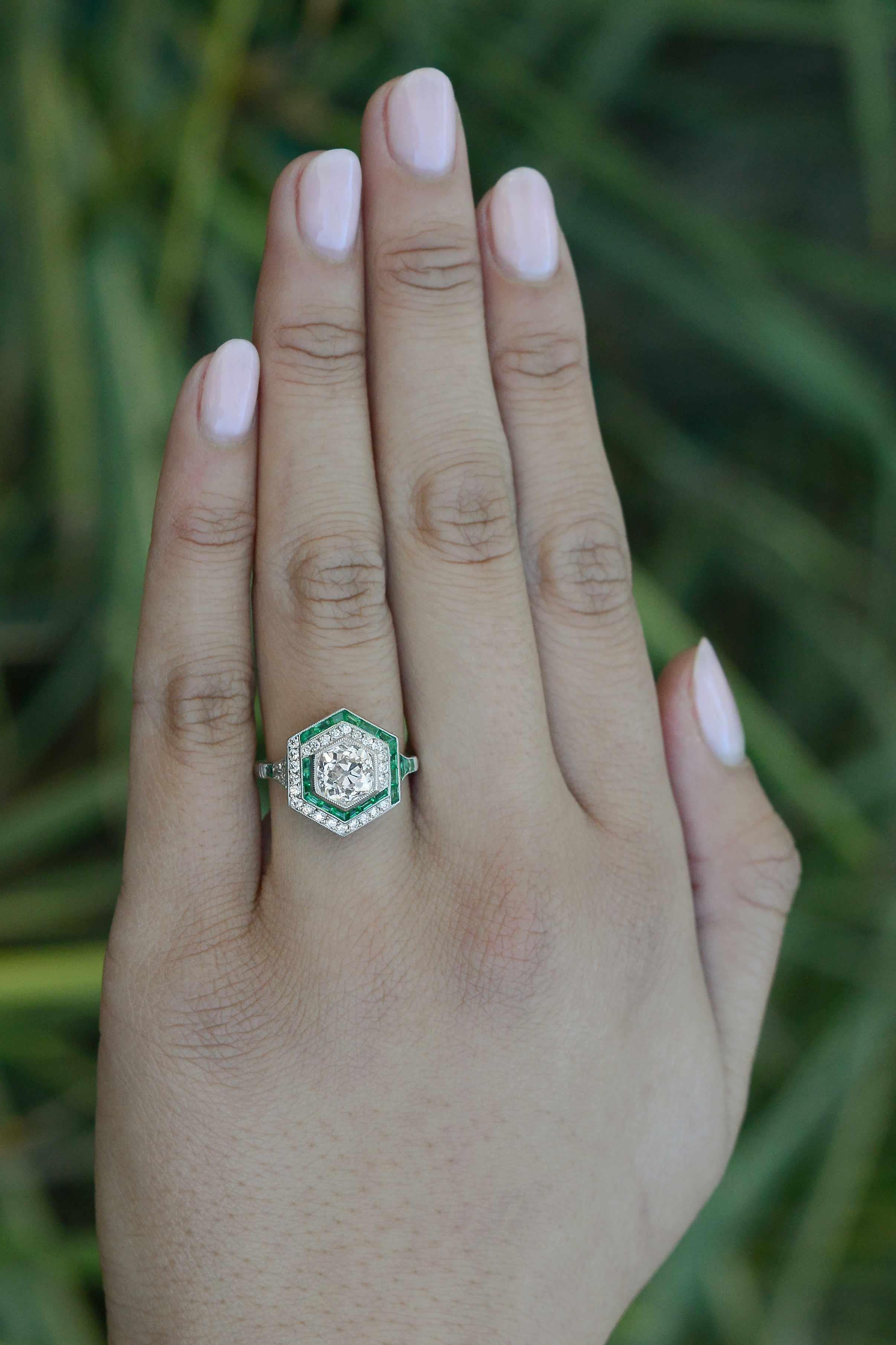 This gorgeous asymmetrical emerald halo diamond engagement ring is a one of a kind treasure that is truly jaw dropping. Hand fabricated in the manner of the Art Deco era of platinum using old world techniques and tools, our jeweler has created a