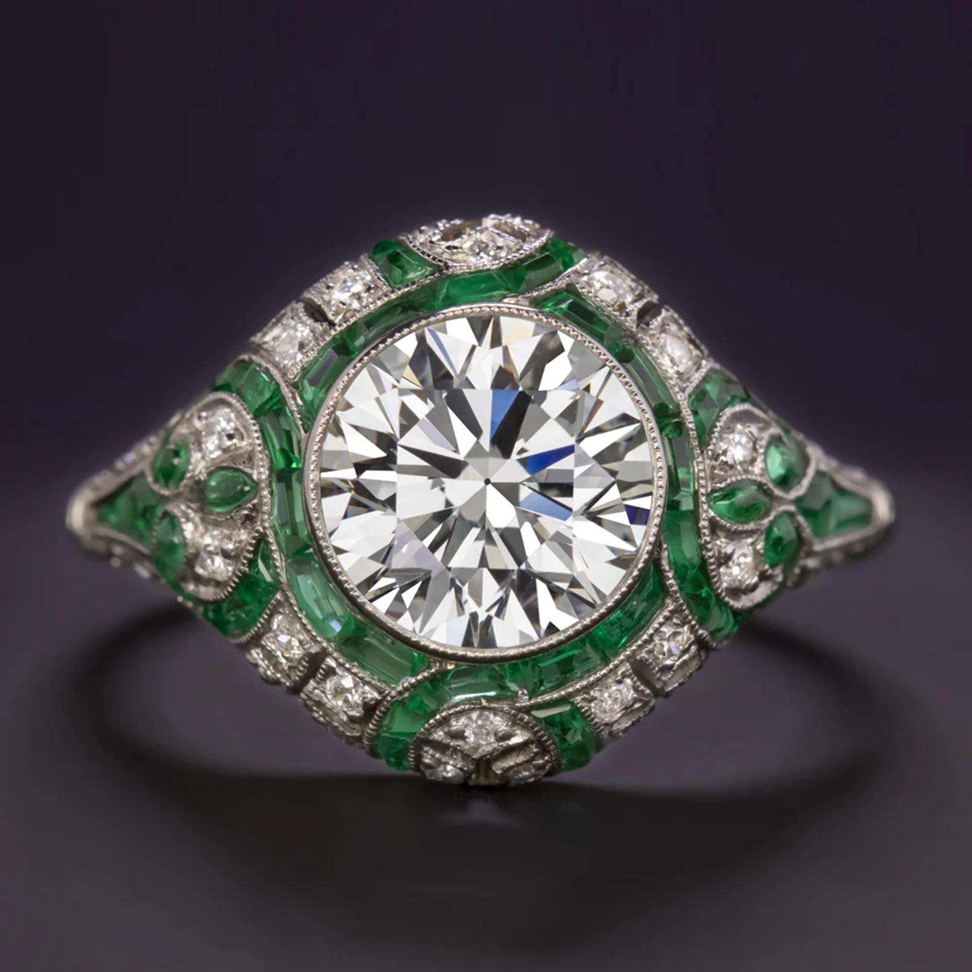 This diamond and emerald ring has a stunning Art Deco style design with an eye catching 1.84ct vintage round cut diamond surrounded by ribbons of custom cut emeralds and glittering diamonds! The setting is handmade and very masterfully crafted with