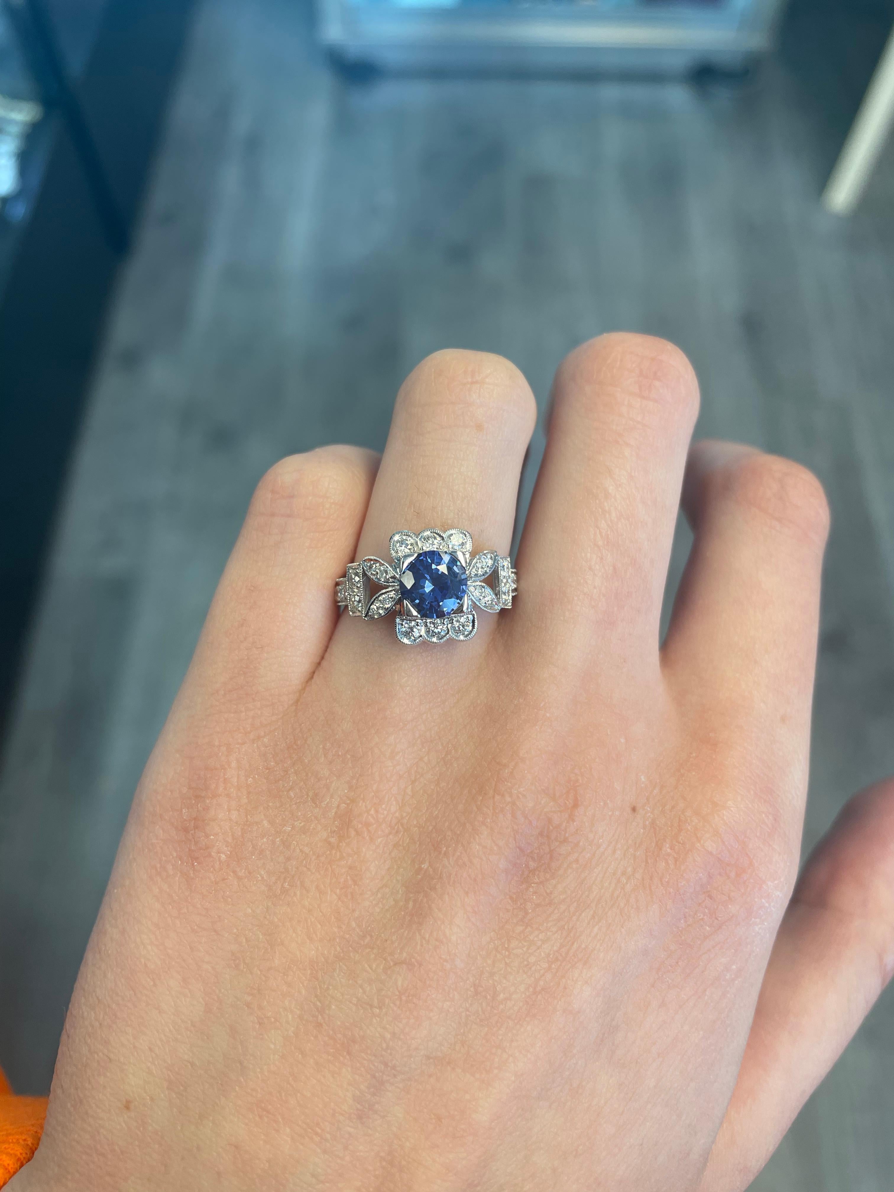 Art Deco style round Ceylon sapphire ring with diamond halo.
1.86 carats total gemstone weight.
Center 1.34 carat round Sri Lankan sapphire heat. Complimented with 0.52 carats of round brilliant diamonds, approximately G/H color and SI clarity. 18k