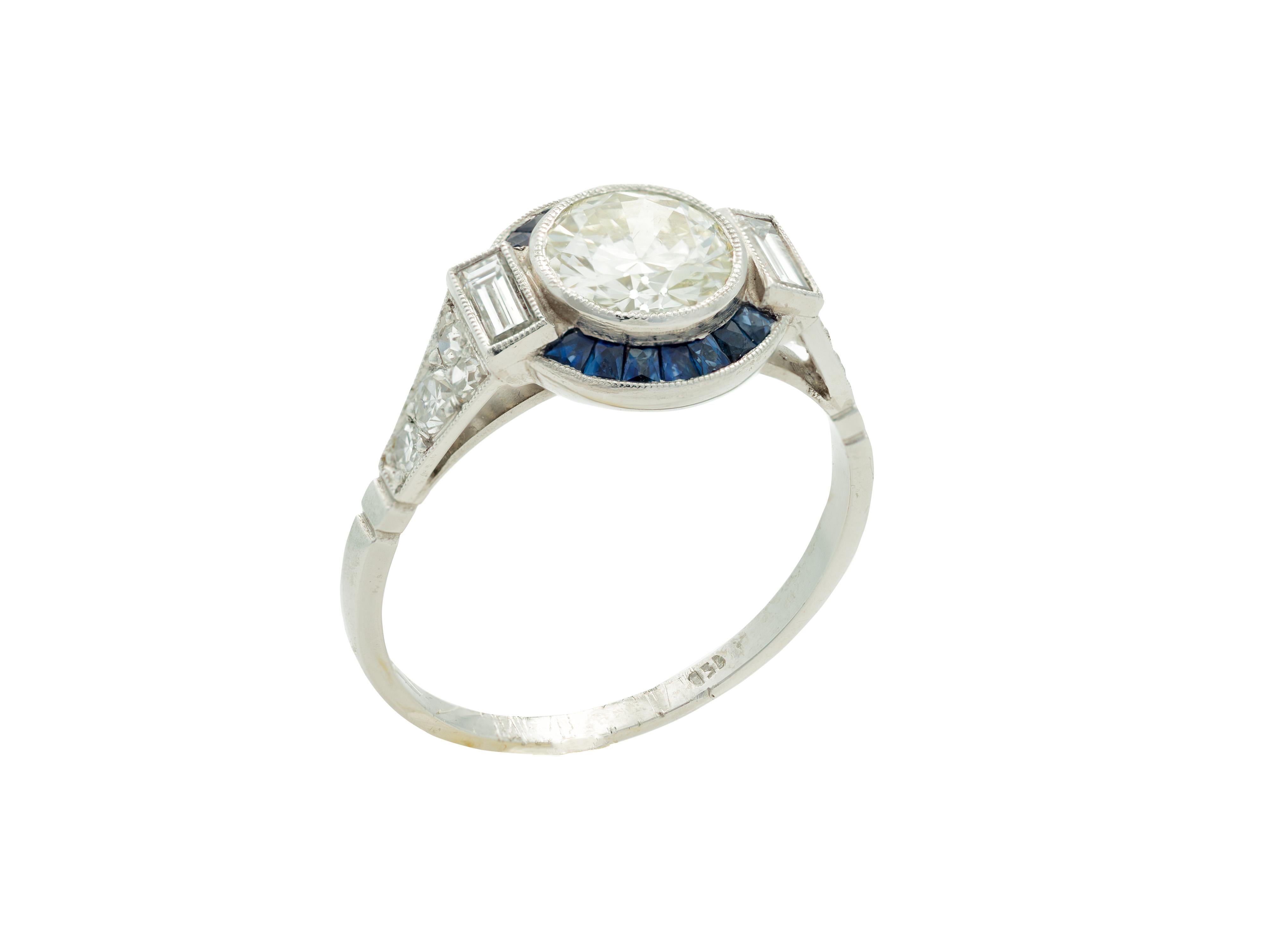 An Art Deco style round European cut Diamond ring with Sapphire halo set in platinum, size 7.5, circa 1960. Created in the USA during the mid-century period, this Art Deco revival ring features a central 1.11 carat round European cut Diamond of H