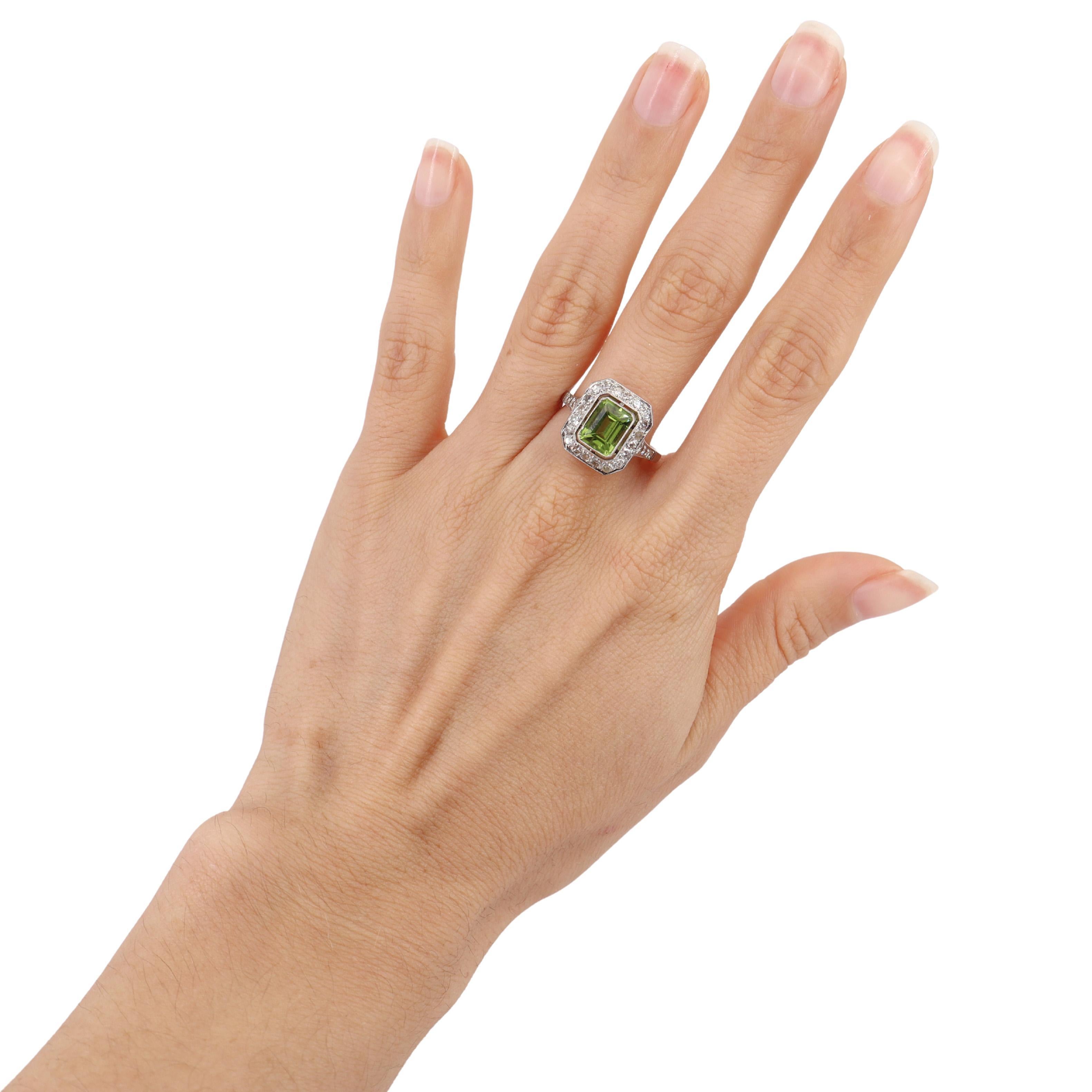 This exquisite cocktail ring showcases a striking emerald-cut peridot, weighing 1.7 carats, radiating a vibrant green hue. Encircling the peridot are single-cut diamonds, totaling 0.56 carats, with a color grade of H and VS1 clarity, adding a