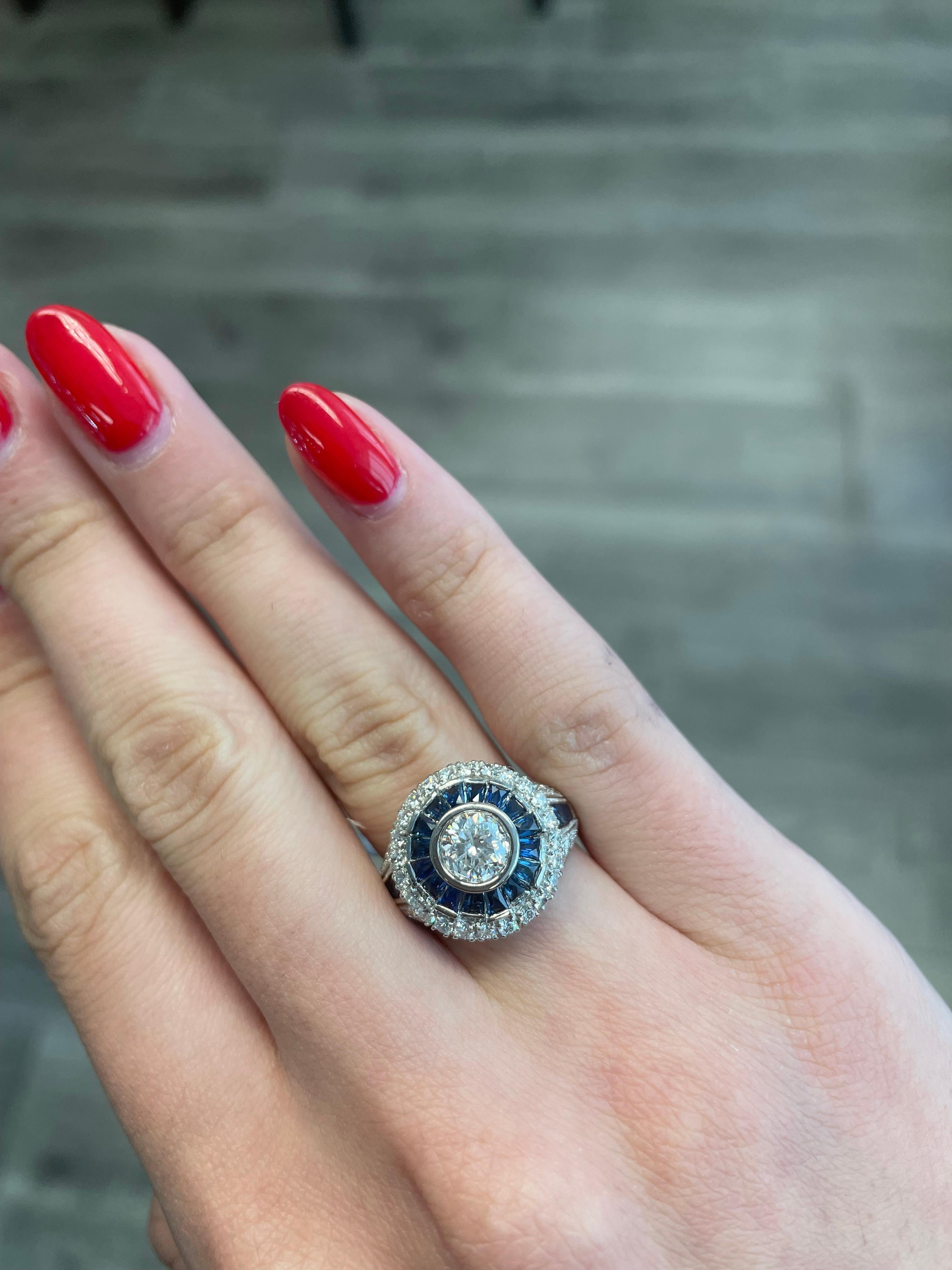 Art Deco inspired ring with a round brilliant cut diamond and French cut sapphires. 
1.00ct center round brilliant cut diamond. Complimented with 0.57ct of round diamonds and 1.25ct of French cut sapphires. 2.82ct total gemstone weight. 18k white