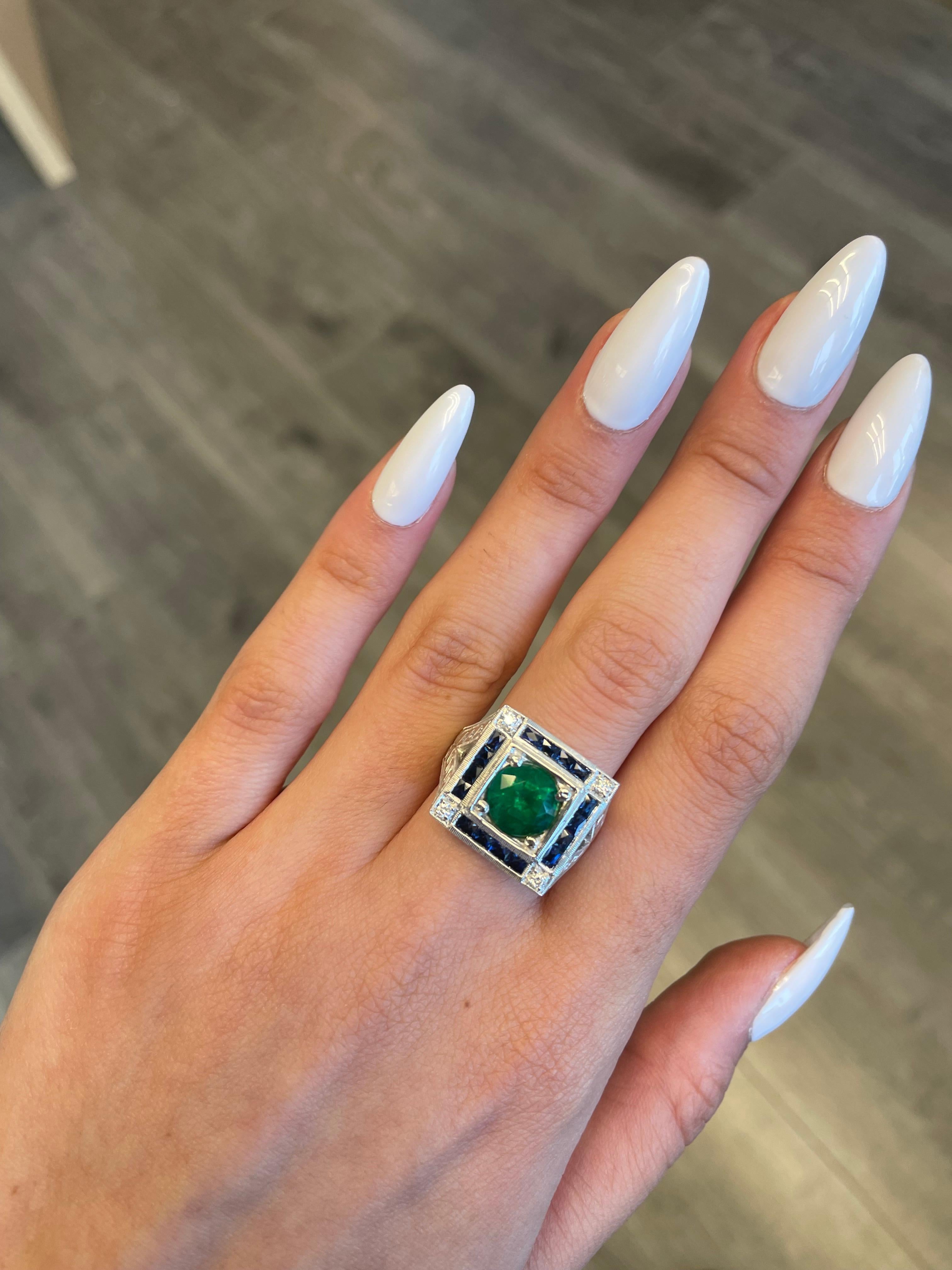 Lovely vintage inspired emerald with sapphires and diamond ring.
2.47 carat round emerald apx F2 complimented with 1.20ct of french cut sapphires heat and 0.10ct of round brilliant diamonds. Approximately G/H color and SI clarity. 18-karat white